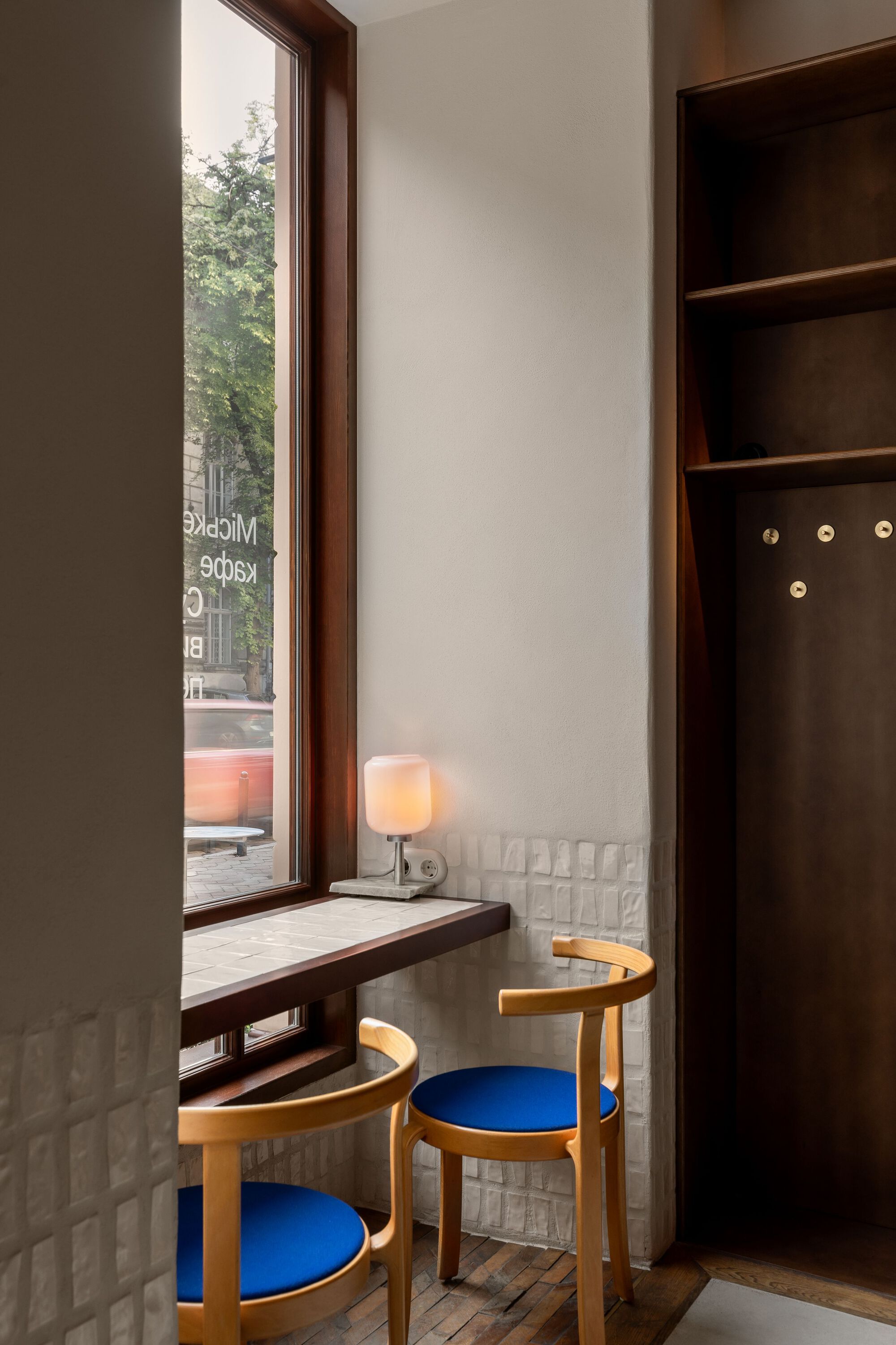 Window seat with dark wood frame, white quilted tile wainscoting and wooden chairs with blue cushions