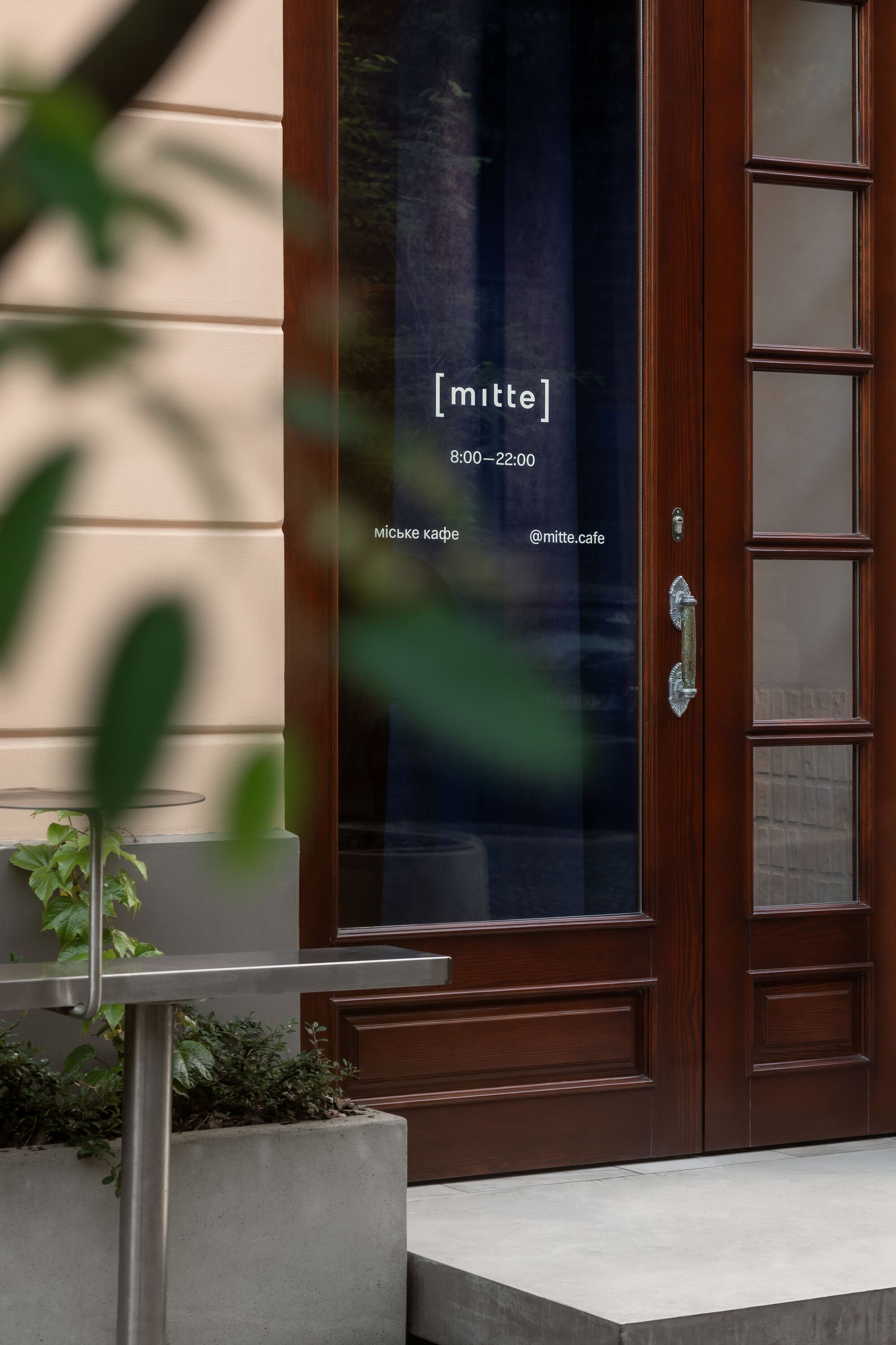 Timber framed entrance door with glazed panel, flanked by potted plants in afternoon light