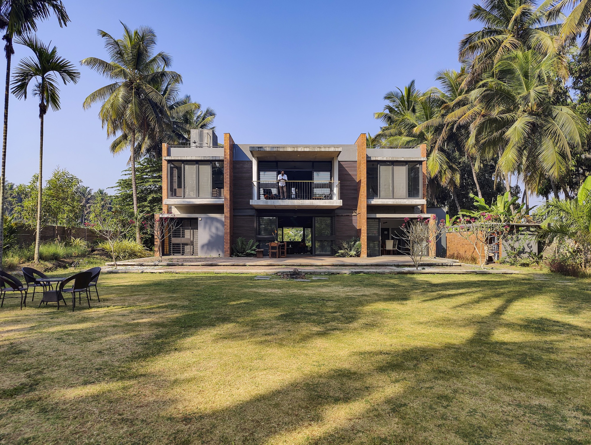 Garden facade with timber and white plaster volumes framed by towering palms under a clear sky