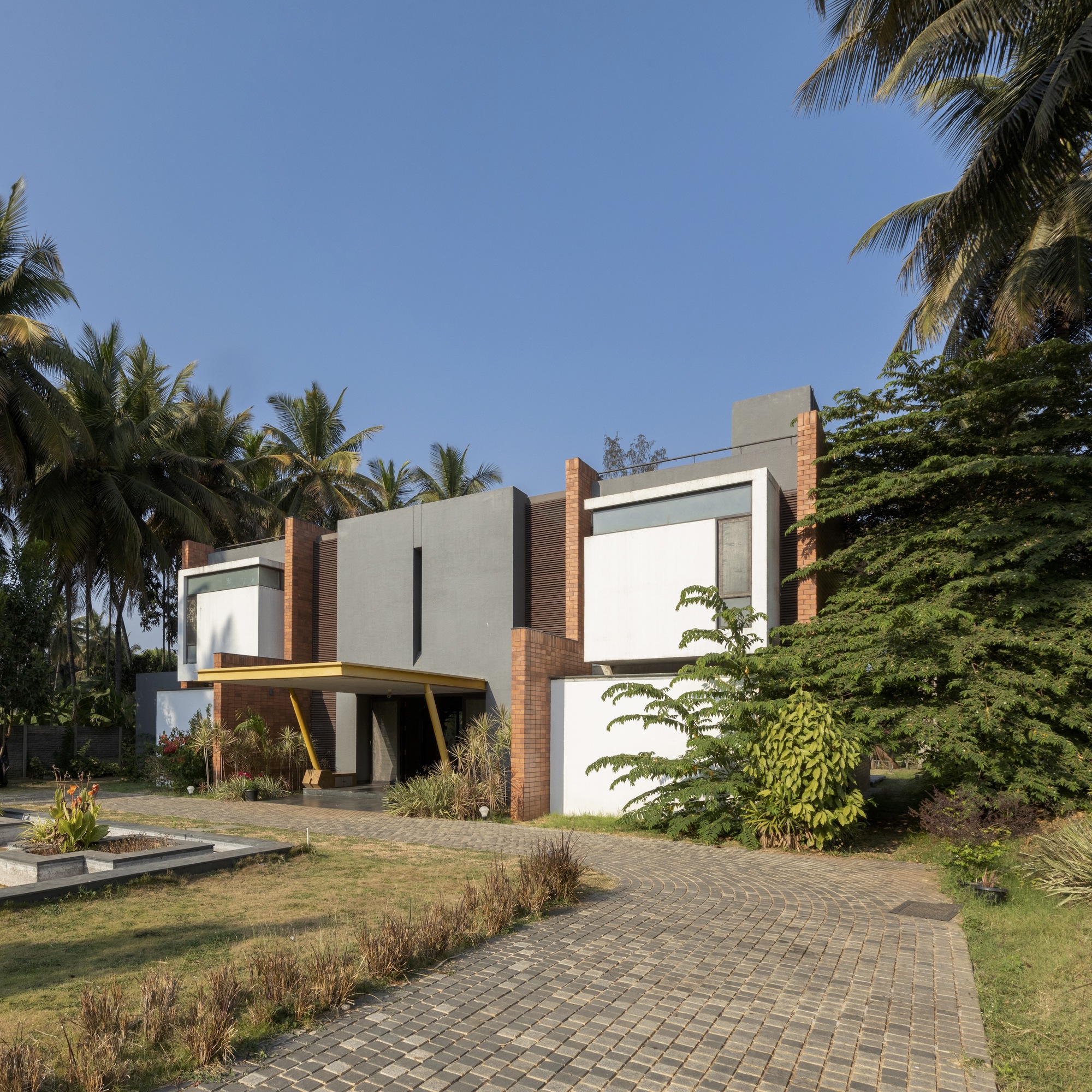 Angled view of the entrance with brick paving and angled yellow canopy amid tropical vegetation