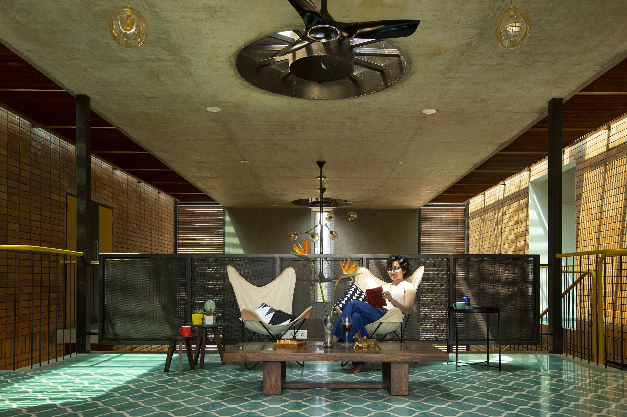 Upper living area with green mosaic floor, slatted timber screens and a seated figure beneath ceiling fans