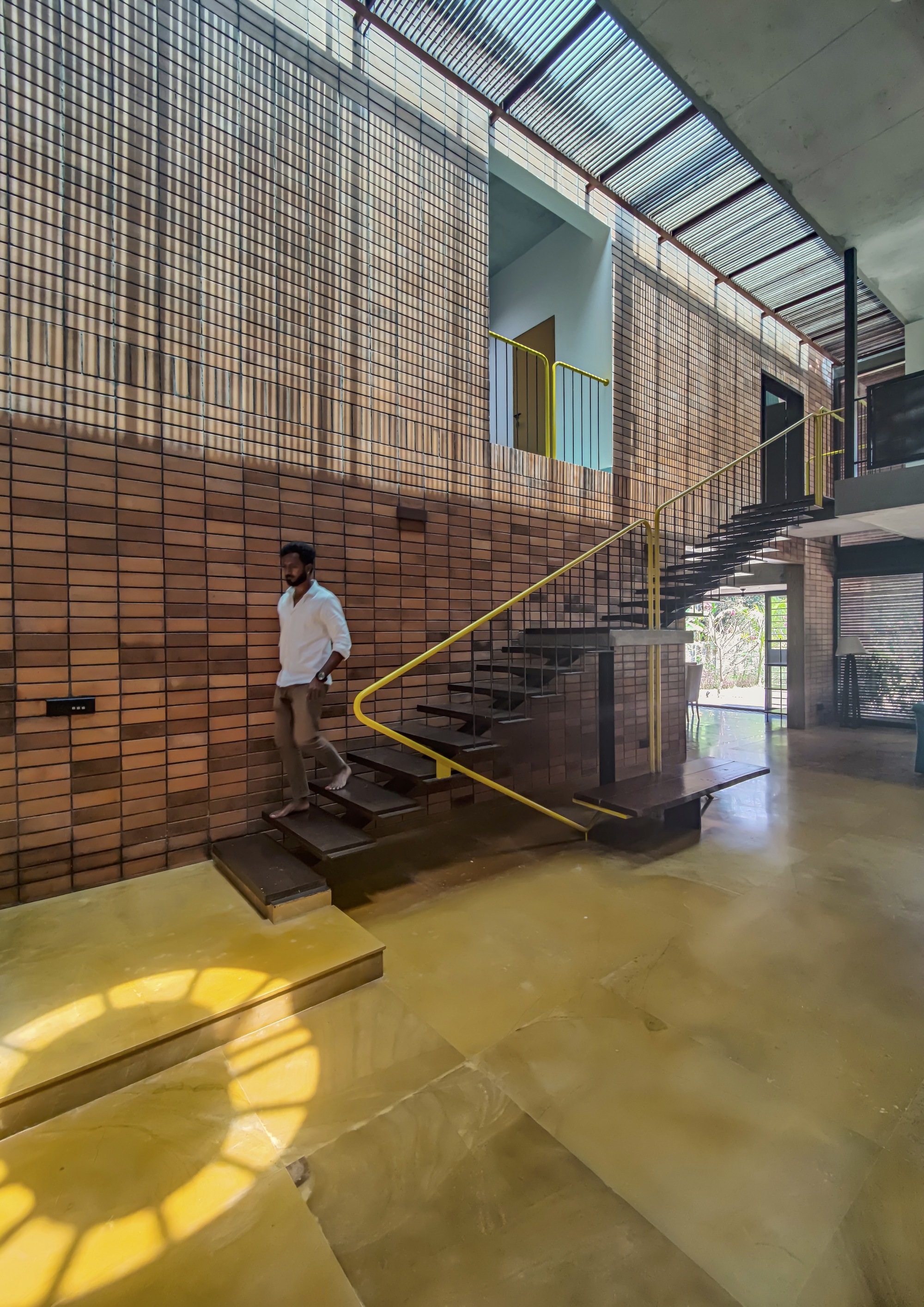 Cantilevered staircase with yellow metal handrail against a terracotta tile wall with a person descending