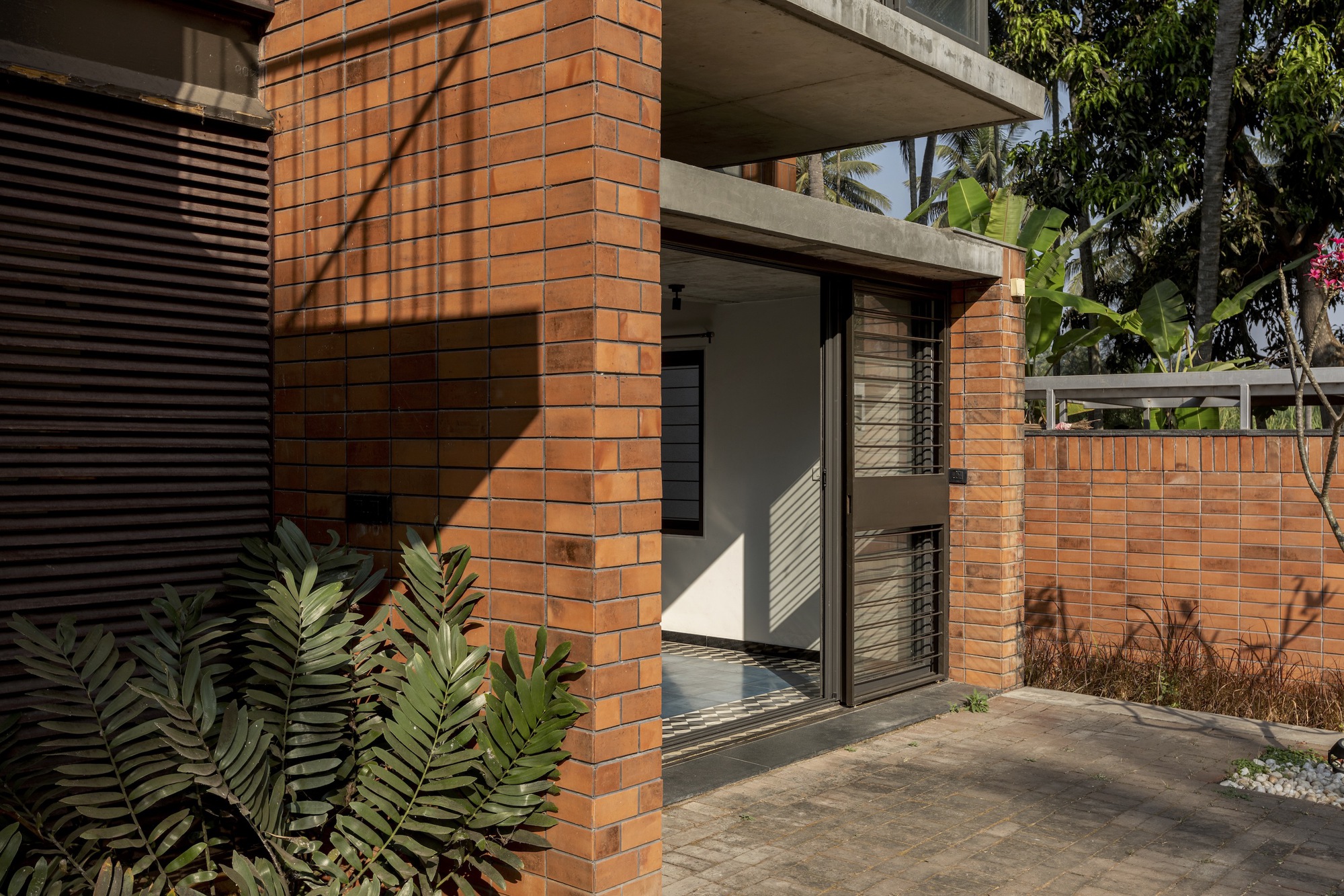 Terracotta brick column and entry threshold with concrete canopy above and morning sunlight on the courtyard