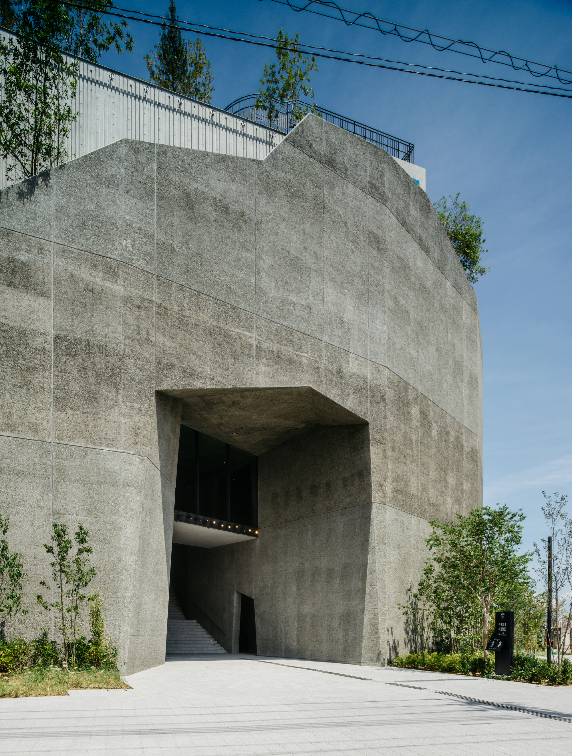 Concrete entrance portal with deep recessed opening and visible staircase under a clear blue sky