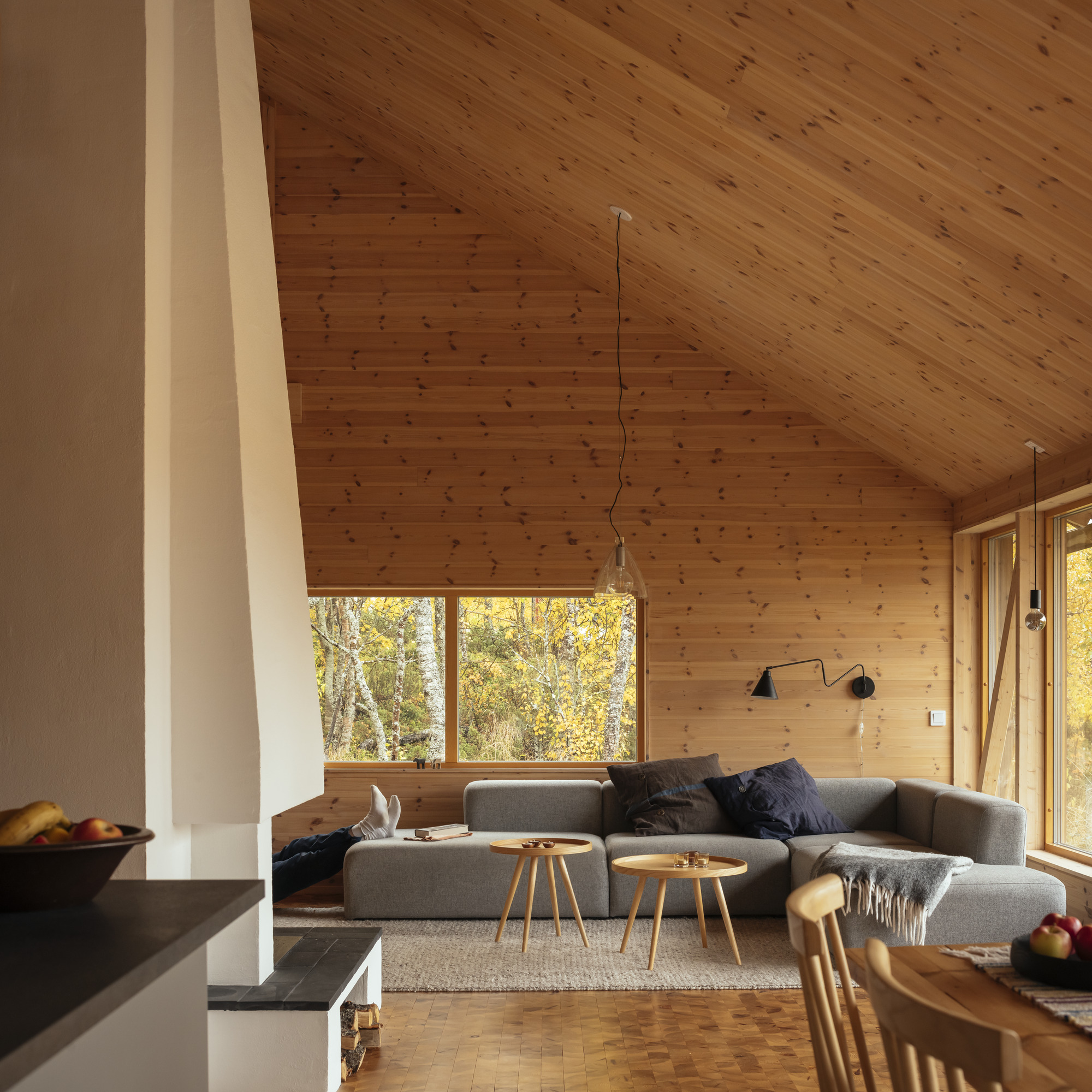 Living room with vaulted tongue-and-groove ceiling, grey sofa, and pendant lights under warm afternoon sun