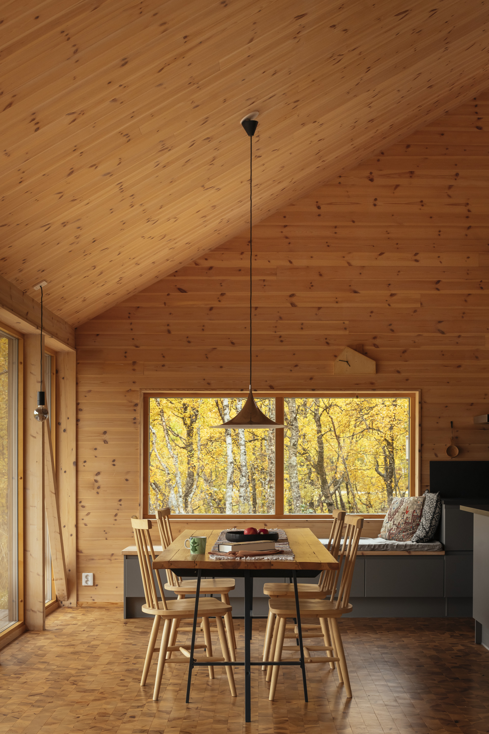Dining area with wood plank ceiling and horizontal window framing yellow autumn birch trees