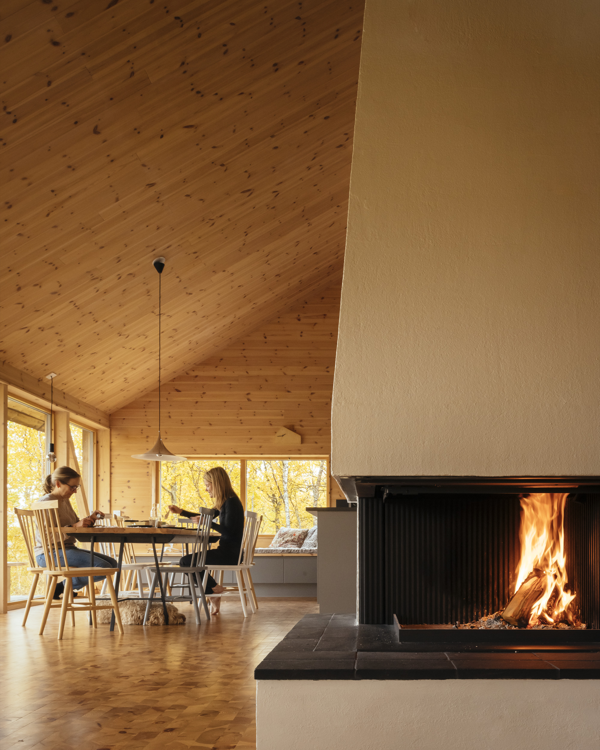 Two people seated at the dining table beside a black metal fireplace with active flames