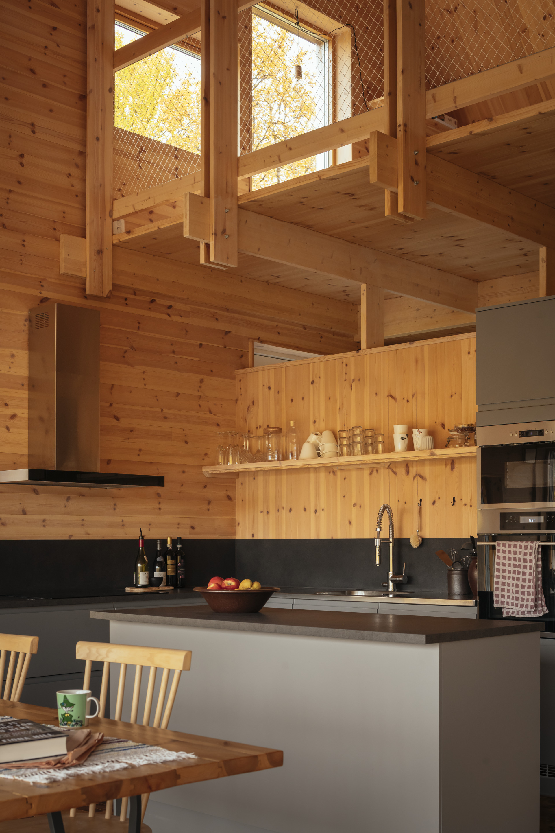 Kitchen island with dark countertop below exposed timber beams and mezzanine level with diamond mesh railing