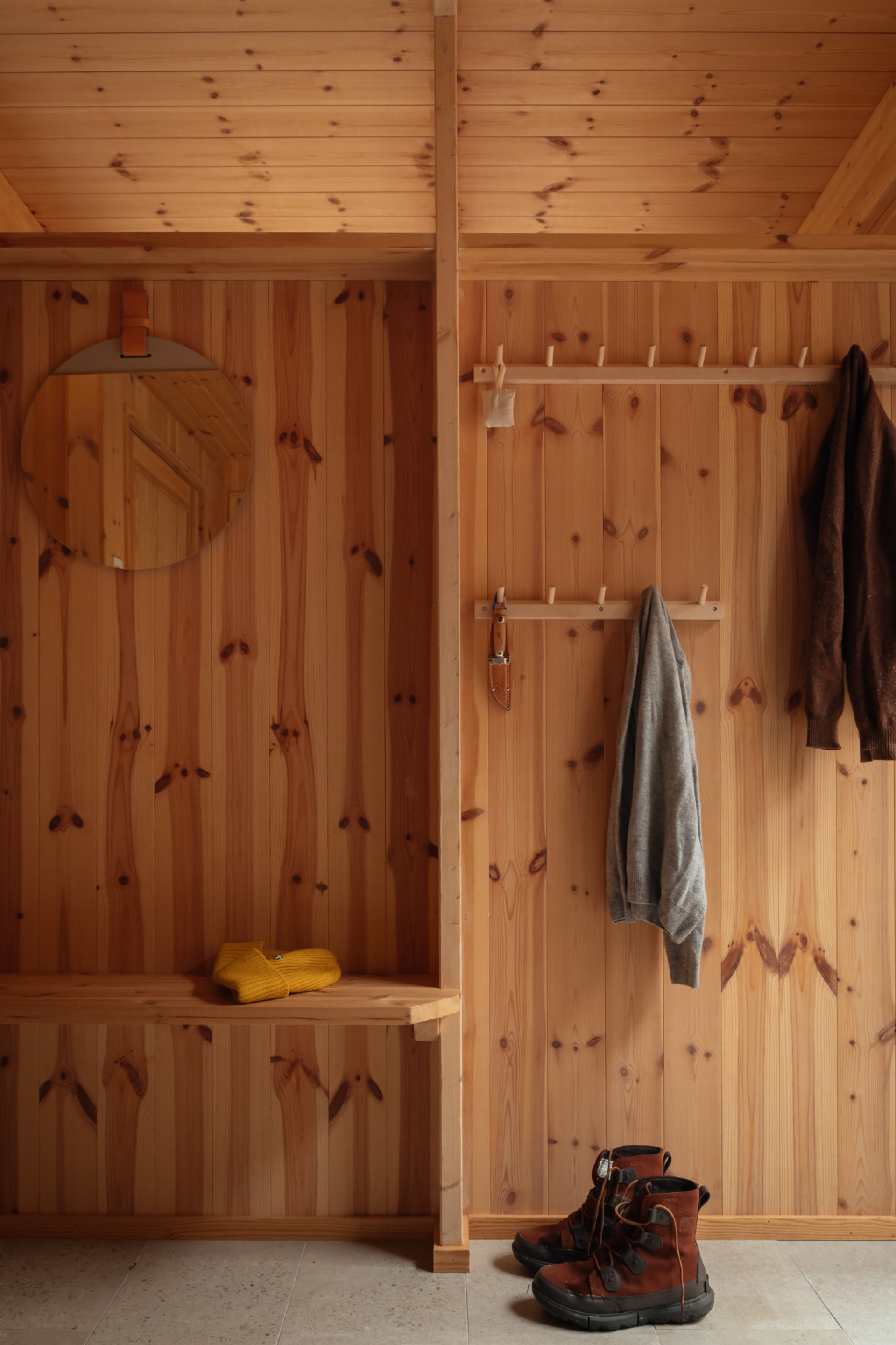 Knotty pine entryway wall with mounted mirror, coat hooks, towel, and boots on the floor