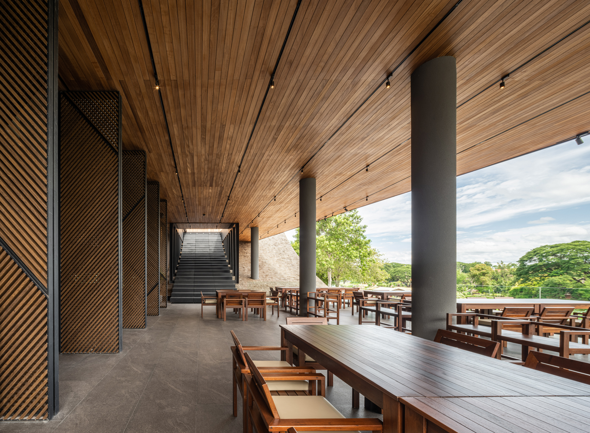 Interior corridor with perforated metal screens and timber ceiling leading to a staircase at the end