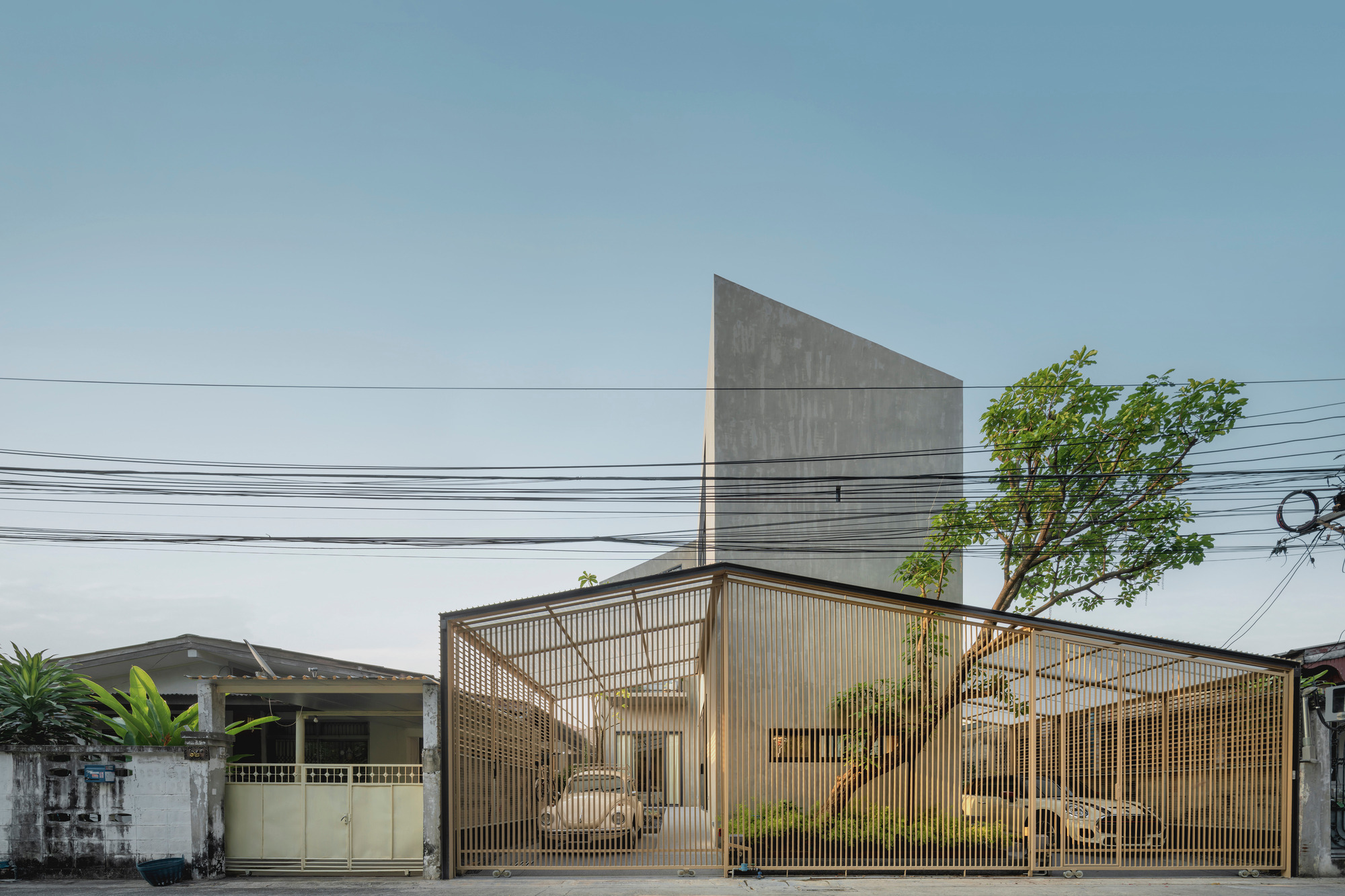 Street view of the translucent corrugated facade with triangular concrete volume rising behind overhead wires