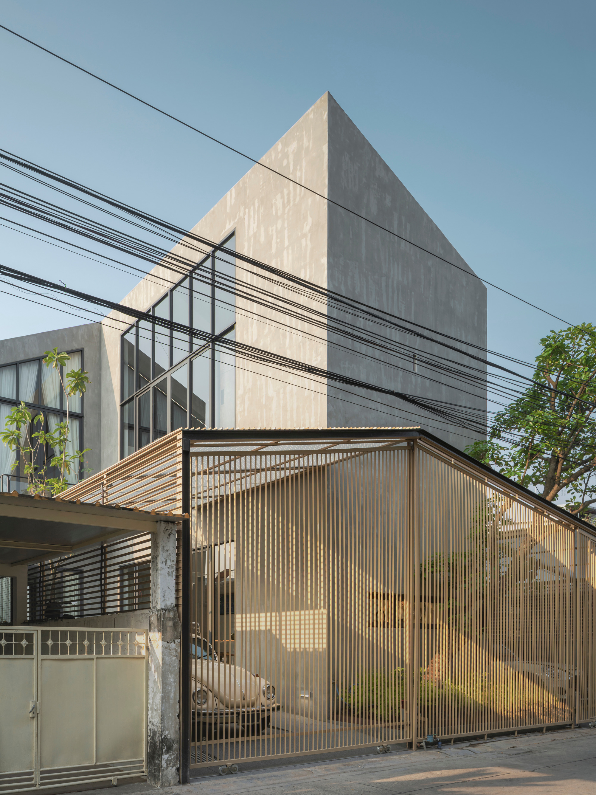 Corner facade showing the angled corrugated screen with stepped concrete mass and power lines crossing the frame