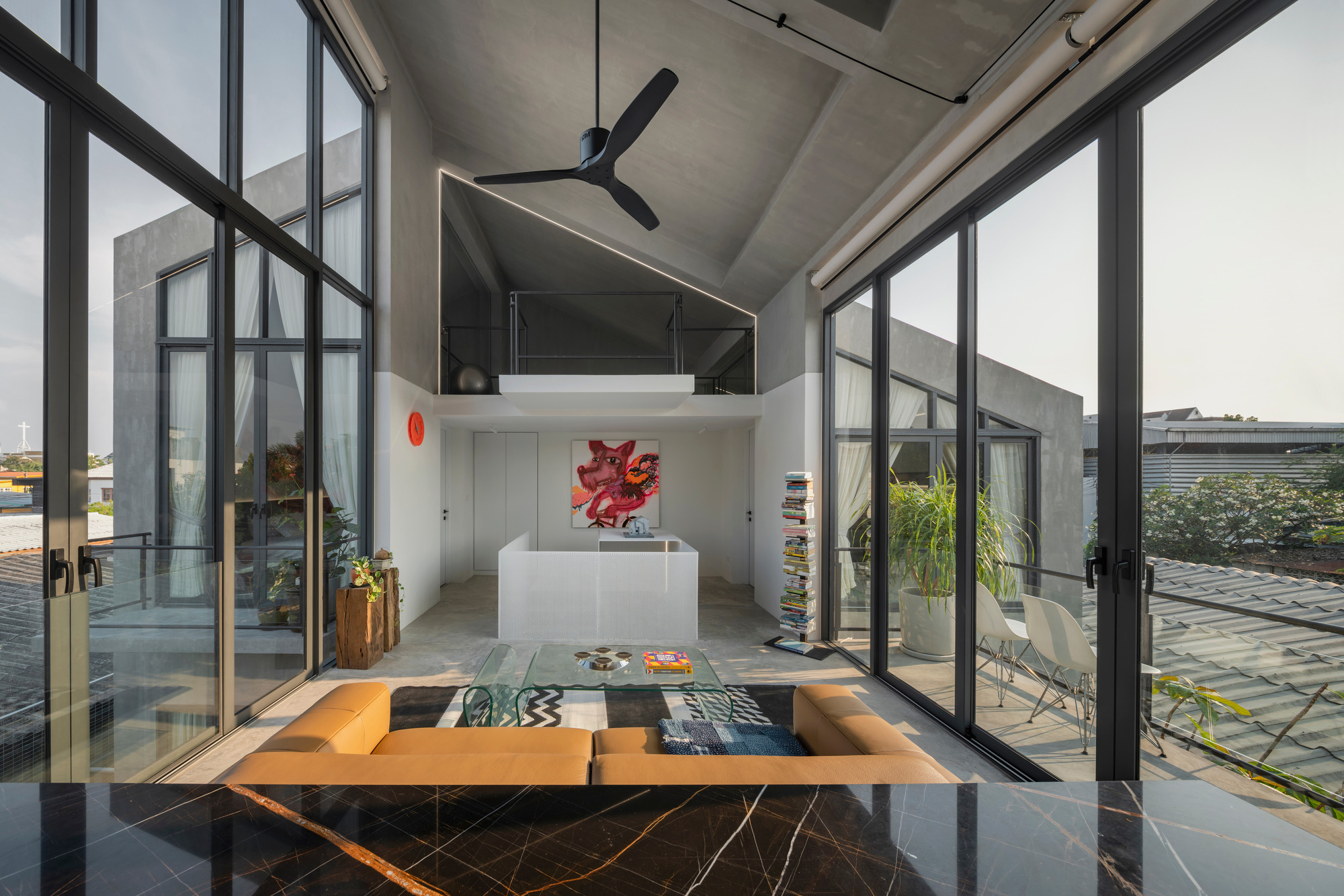 Double-height living space with exposed concrete ceiling, steel-framed glazing, and a low orange seating unit