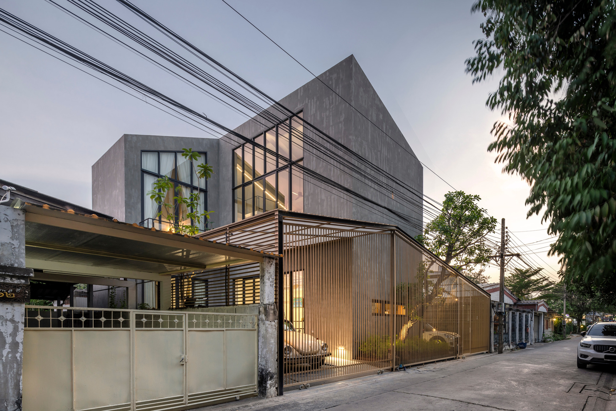Dusk view of the residence with glowing translucent screen, cantilevered terrace, and overhead utility wires