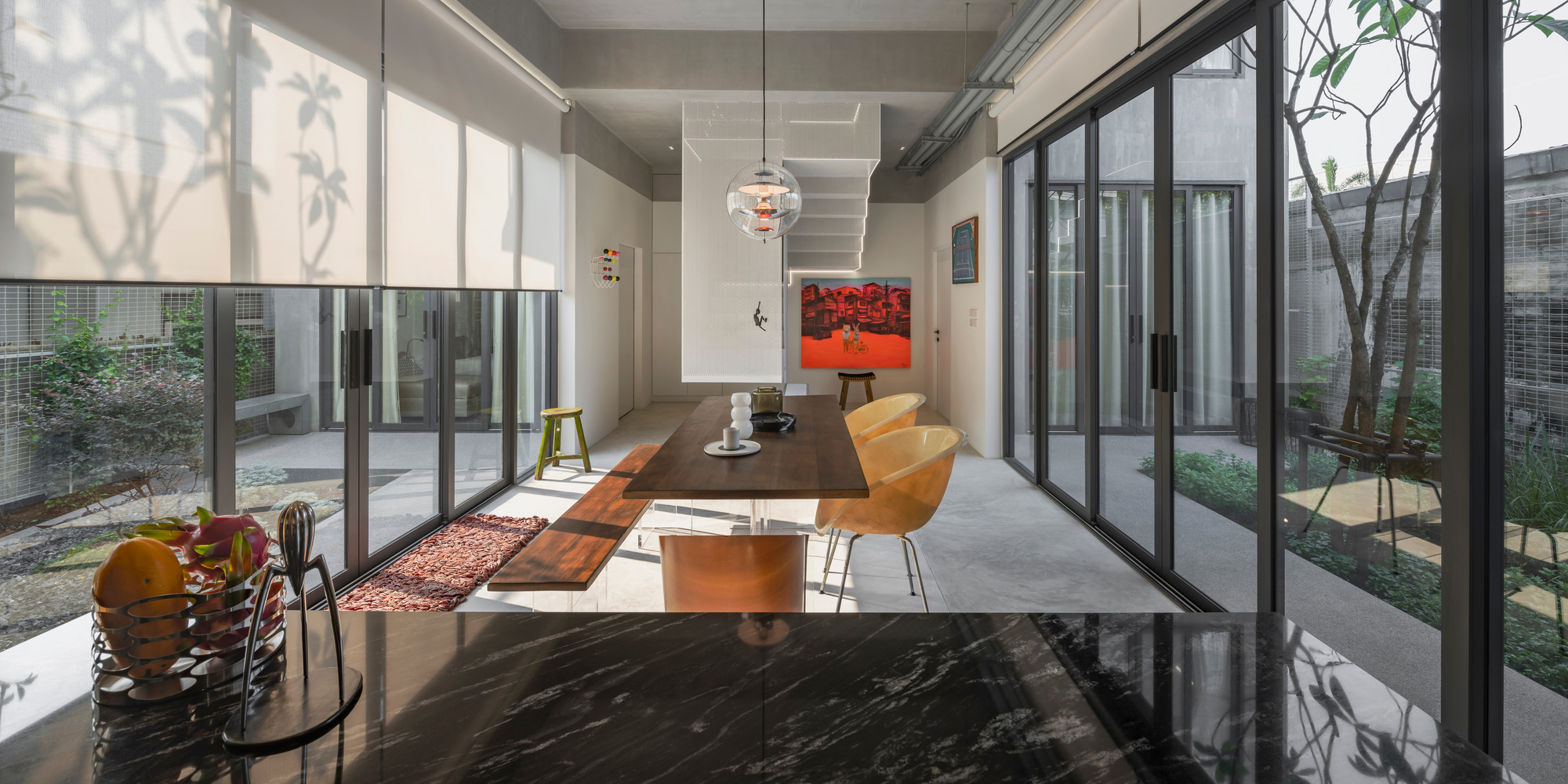 Open-plan dining area with floor-to-ceiling glazing overlooking two planted courtyards under dappled sunlight