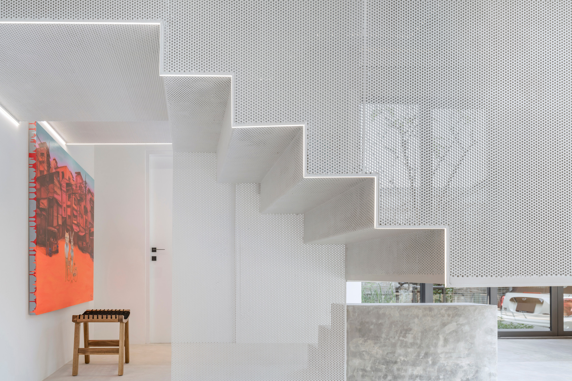 White perforated metal staircase wrapping around a concrete volume beneath integrated linear ceiling lighting