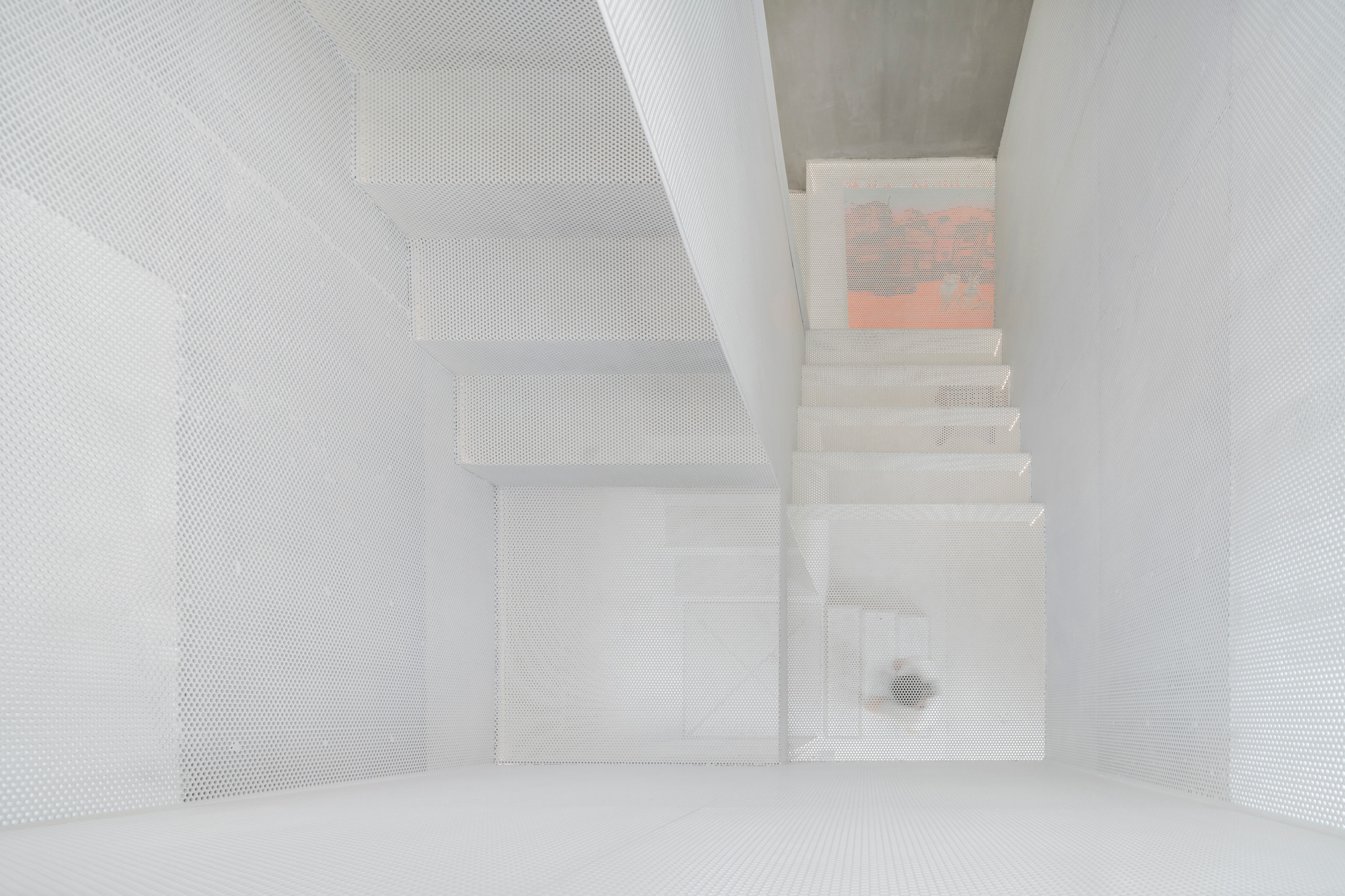 Top-down view of the white perforated metal stairwell with painting visible on upper landing