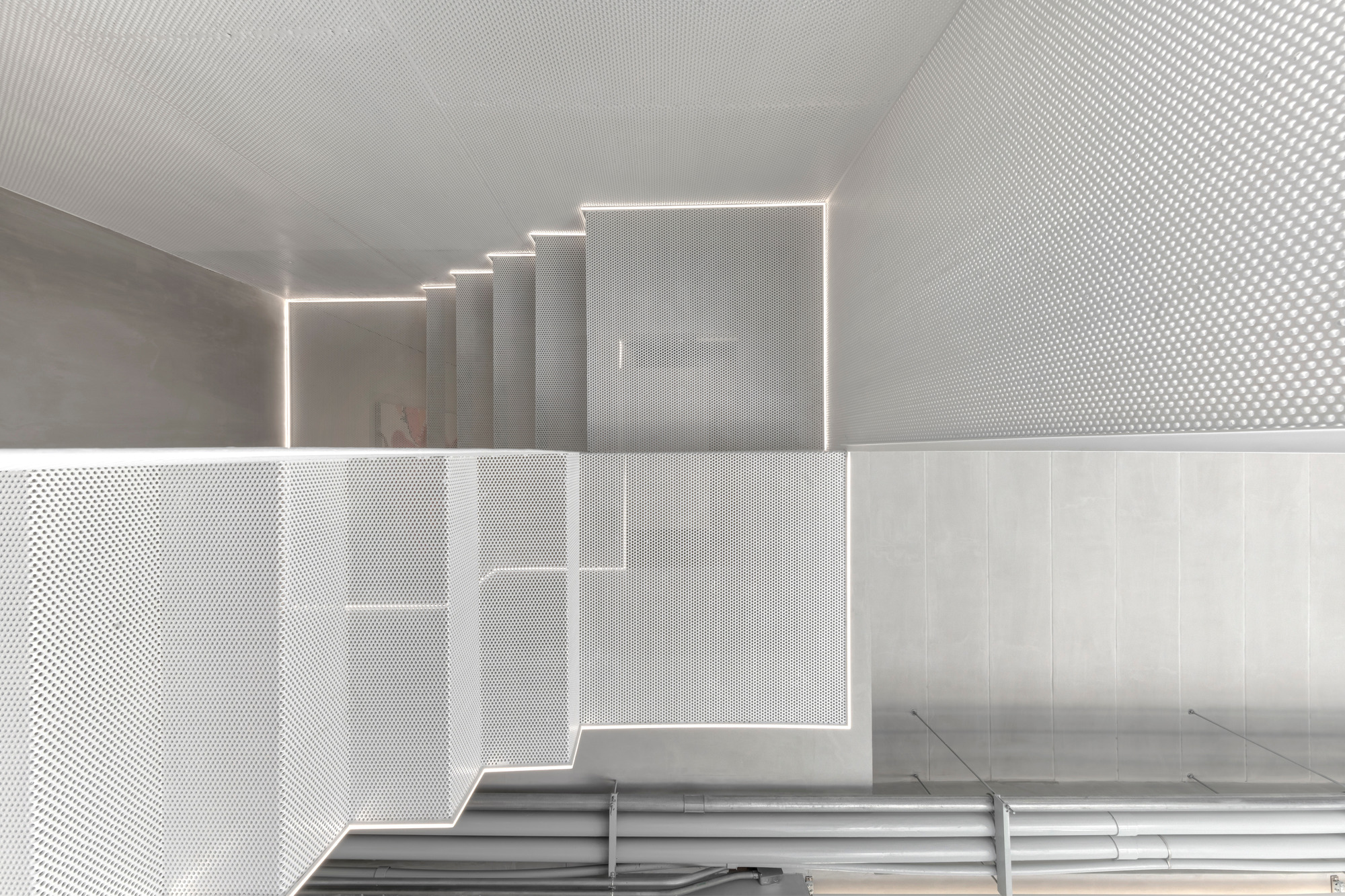 Looking down through the perforated metal floor and stairwell with integrated linear lighting along the edges
