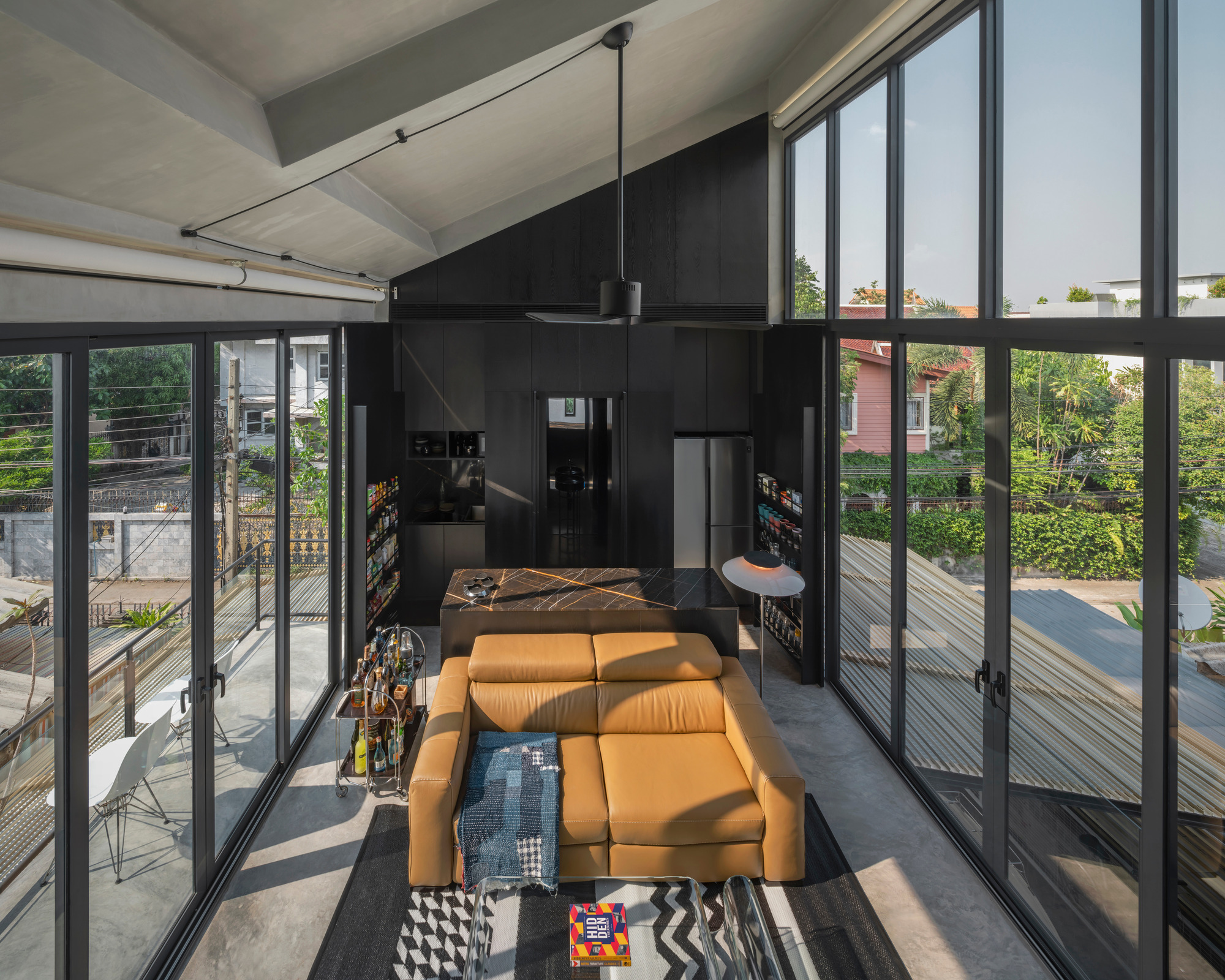 Open living room framed by black steel doors leading to timber decks with afternoon sunlight streaming through