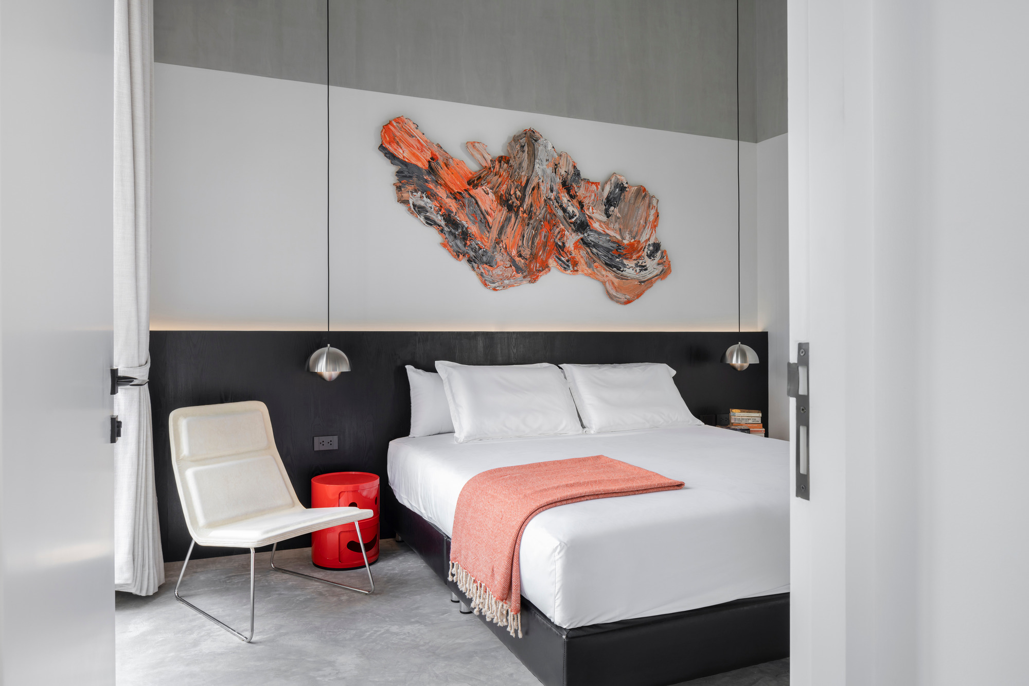 Bedroom with black headboard wall and white linens beneath an abstract coral-toned painting
