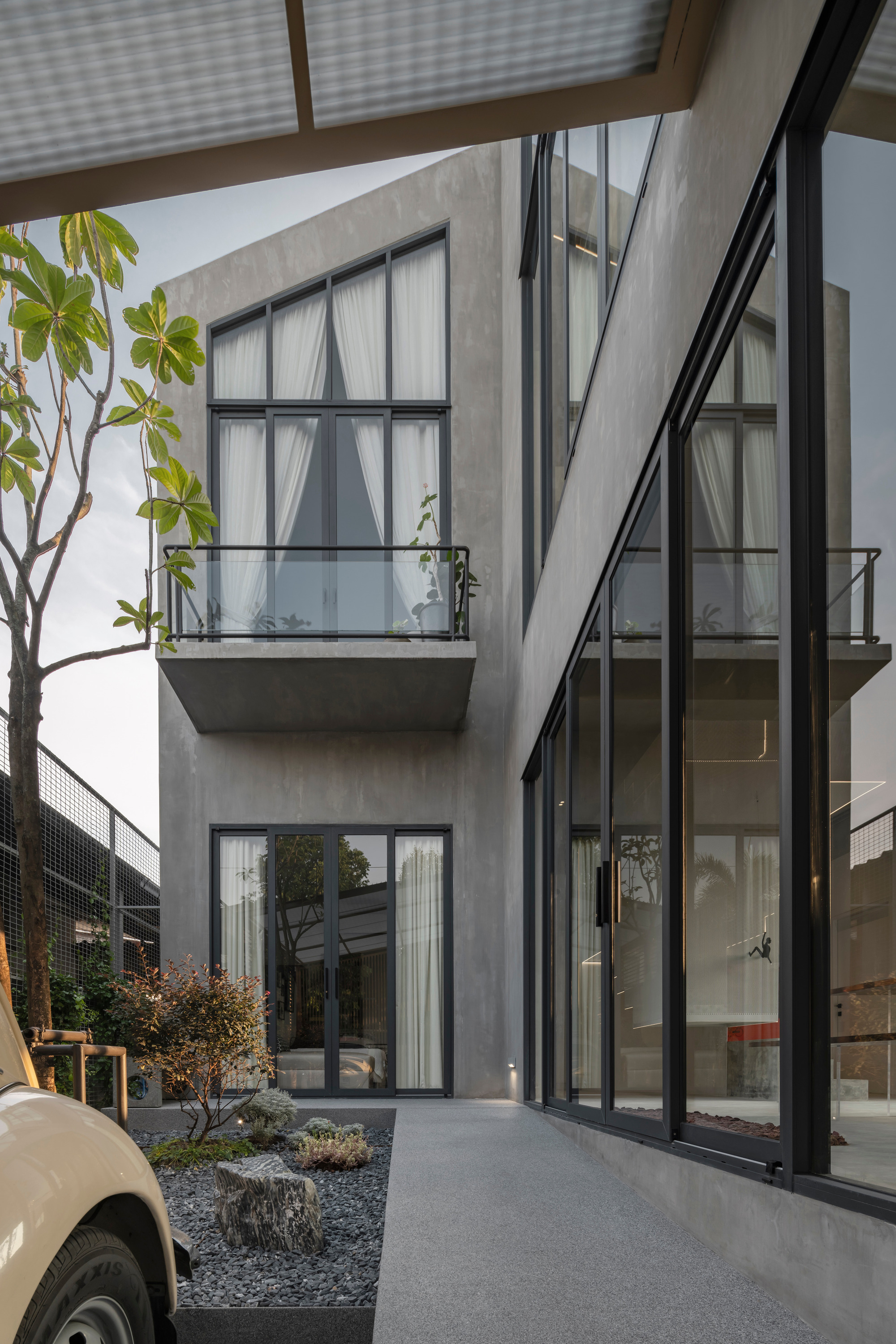 Concrete courtyard with gravel beds and planted trees framed by steel frame windows