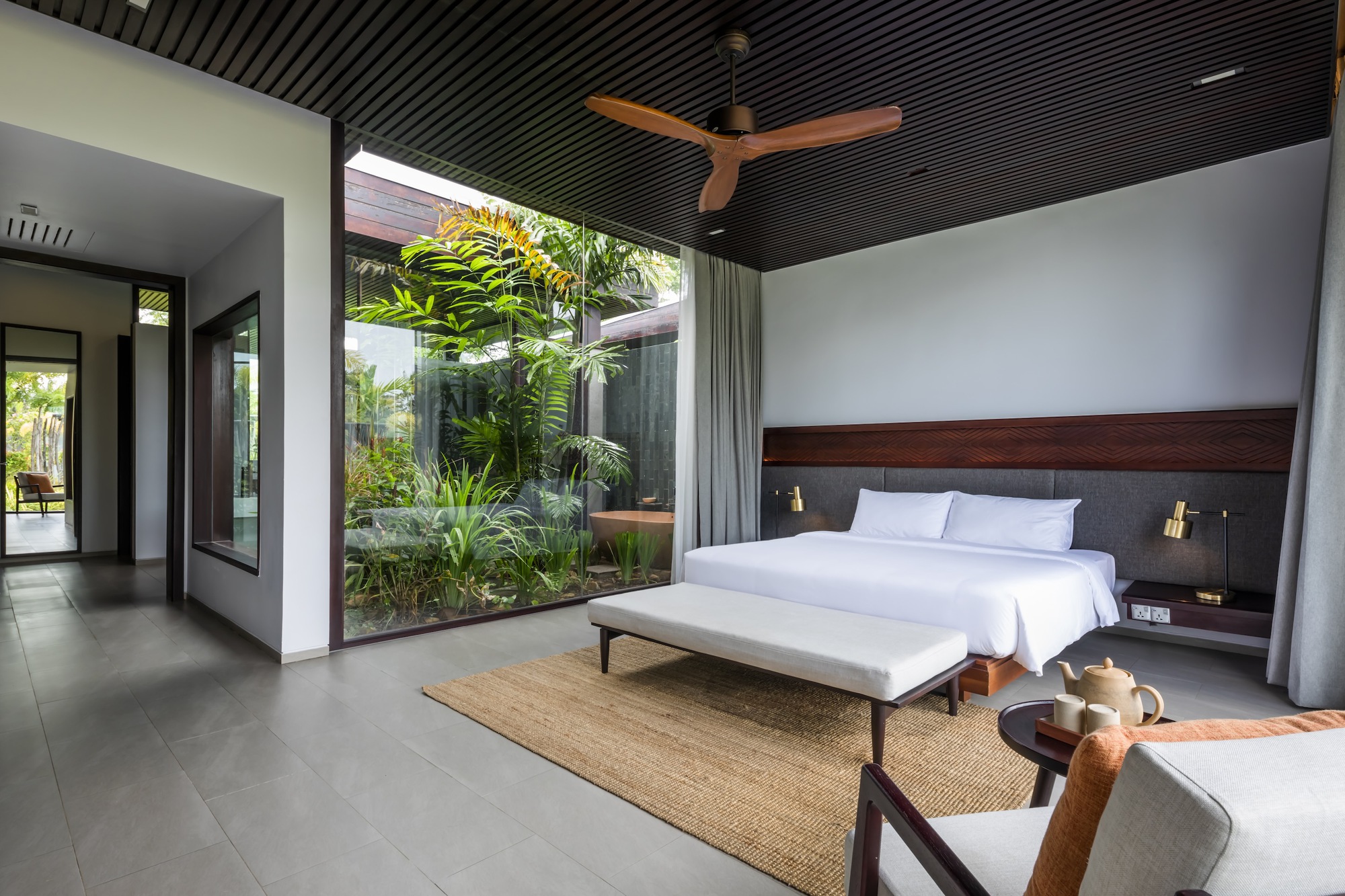 Bedroom interior with slatted black ceiling and full-height glazing opening to a planted courtyard