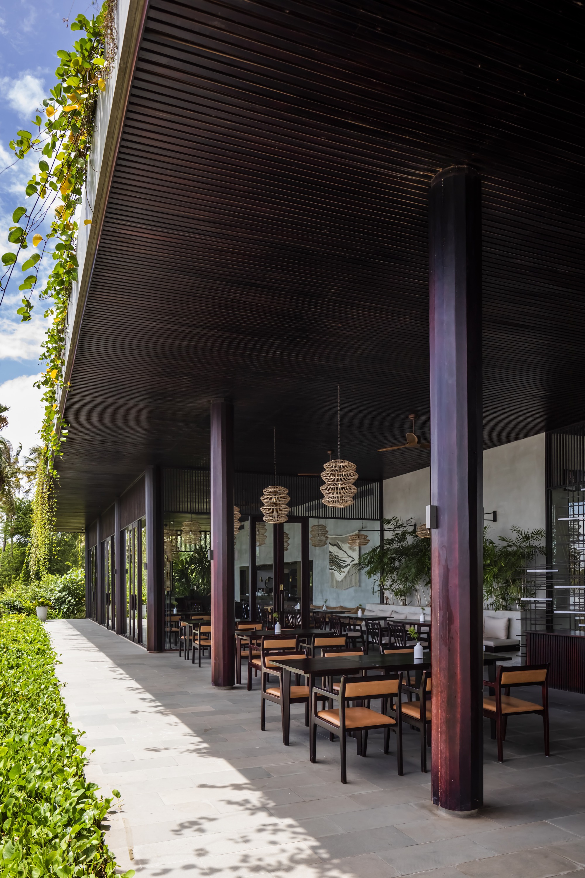 Covered terrace with dark slatted ceiling and steel columns sheltering outdoor dining tables