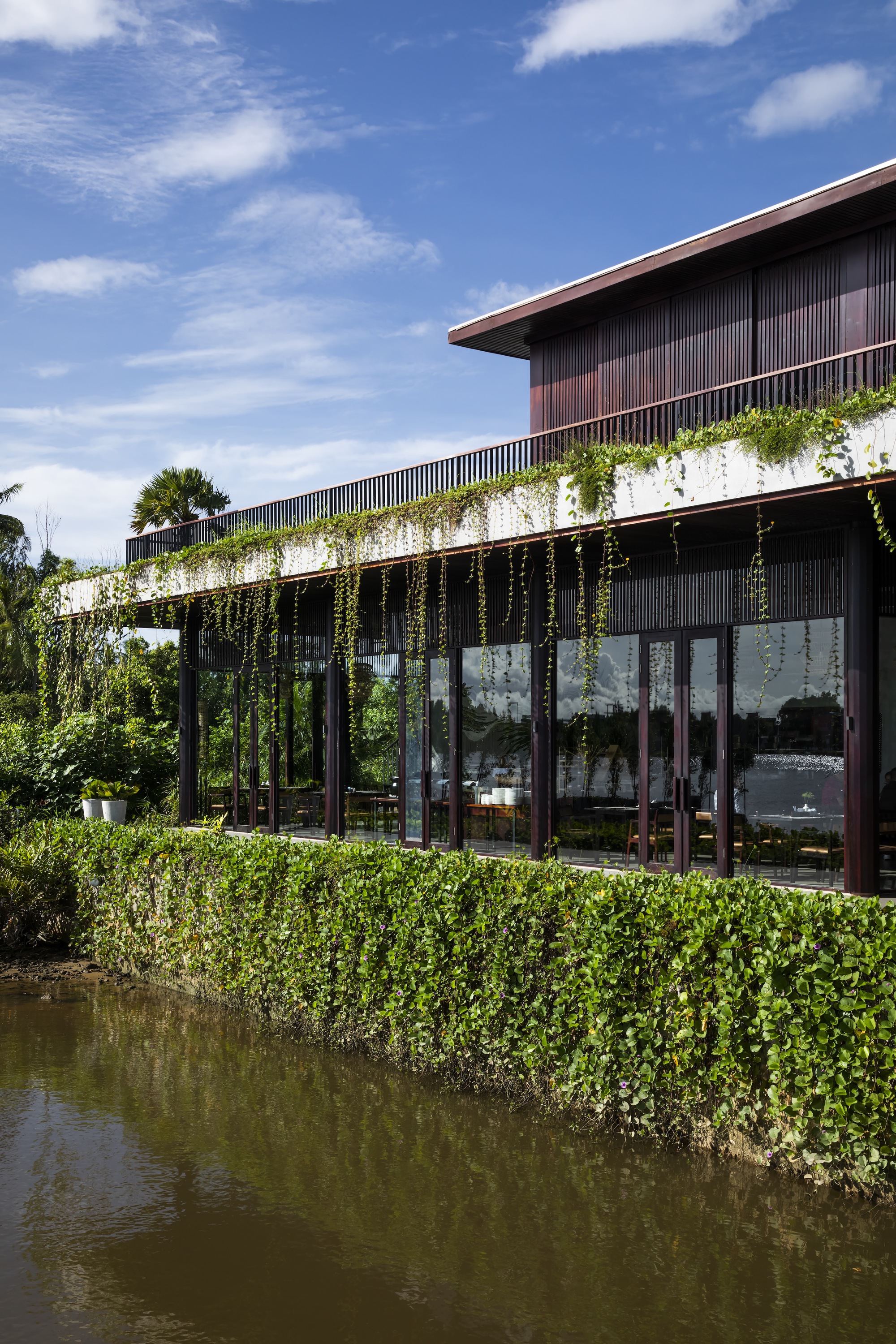 Glass-walled facade with cascading vines along the pergola trellis above a still pond