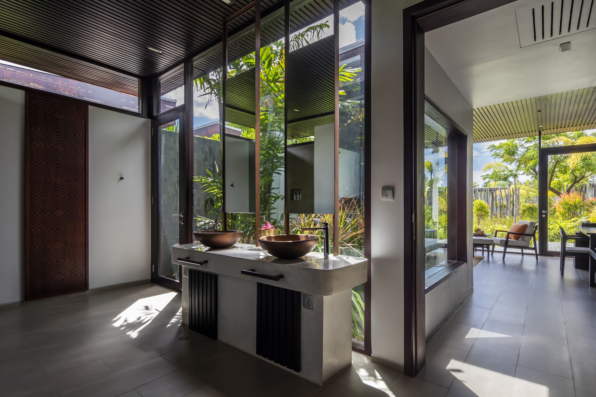Bathroom with copper vessel sinks on floating vanity flanked by glazed courtyards with tropical plants