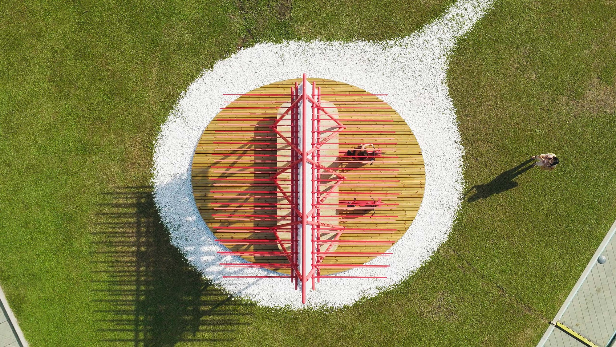 Aerial view of the pavilion on a circular timber deck with white gravel border and a lone pedestrian