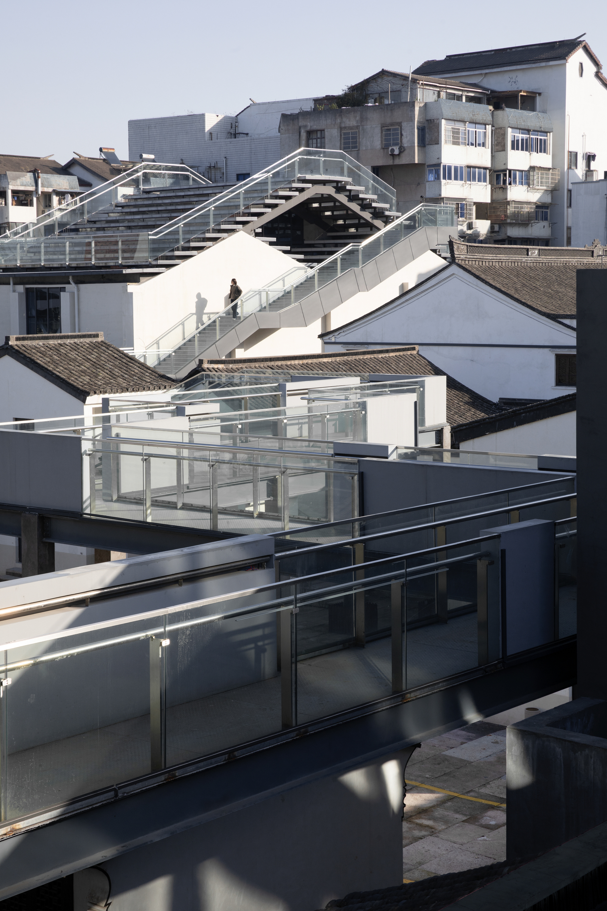 Arched pedestrian bridge spanning between white buildings above traditional pitched roofs in daylight