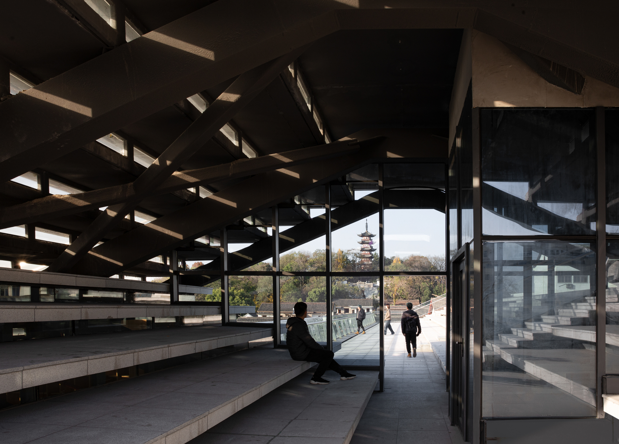 Interior reading room with exposed timber ceiling beams and glass walls framing a pagoda view