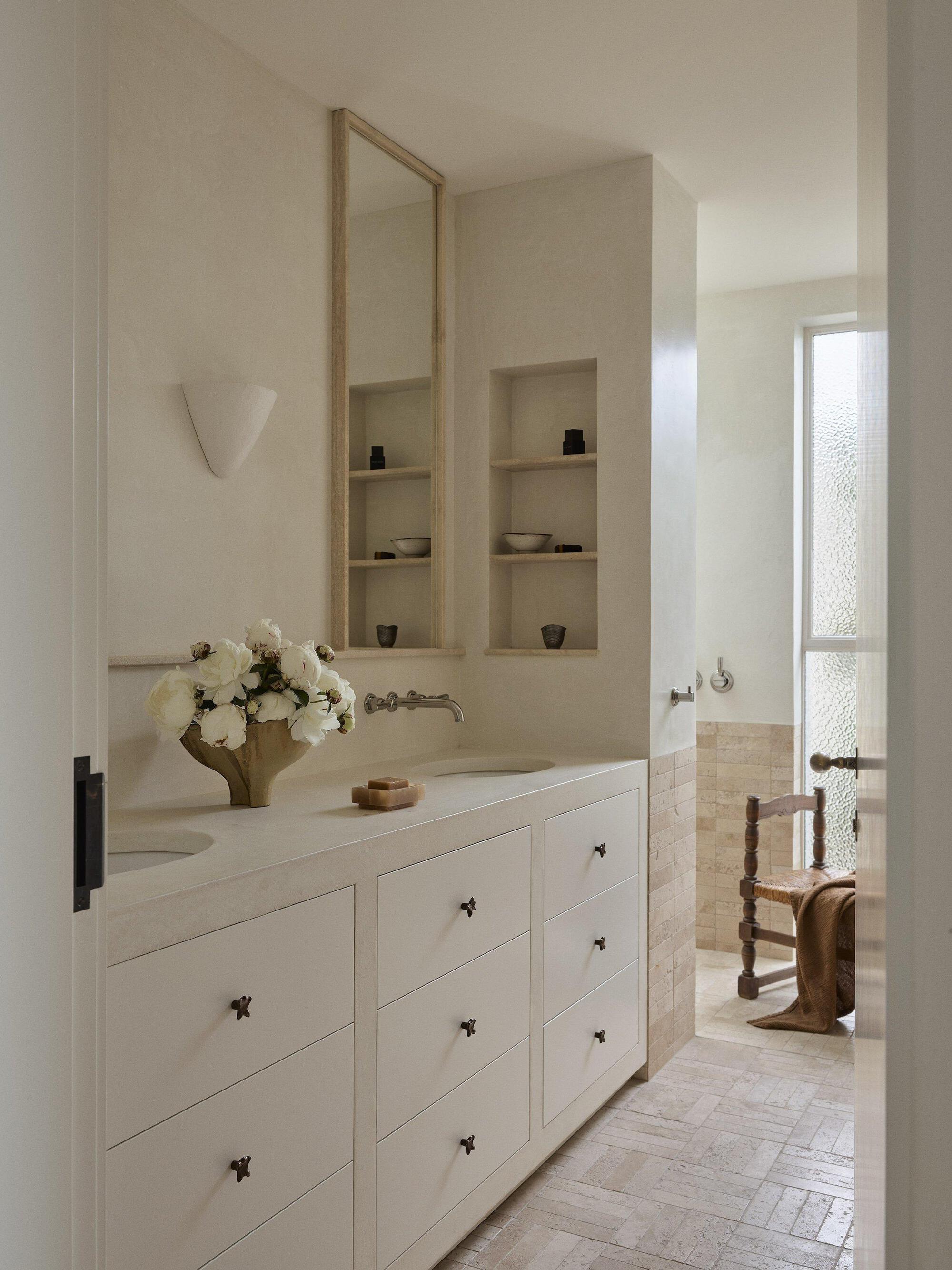 Bathroom vanity with recessed wall niches and a tall mirror beside a textured glass window