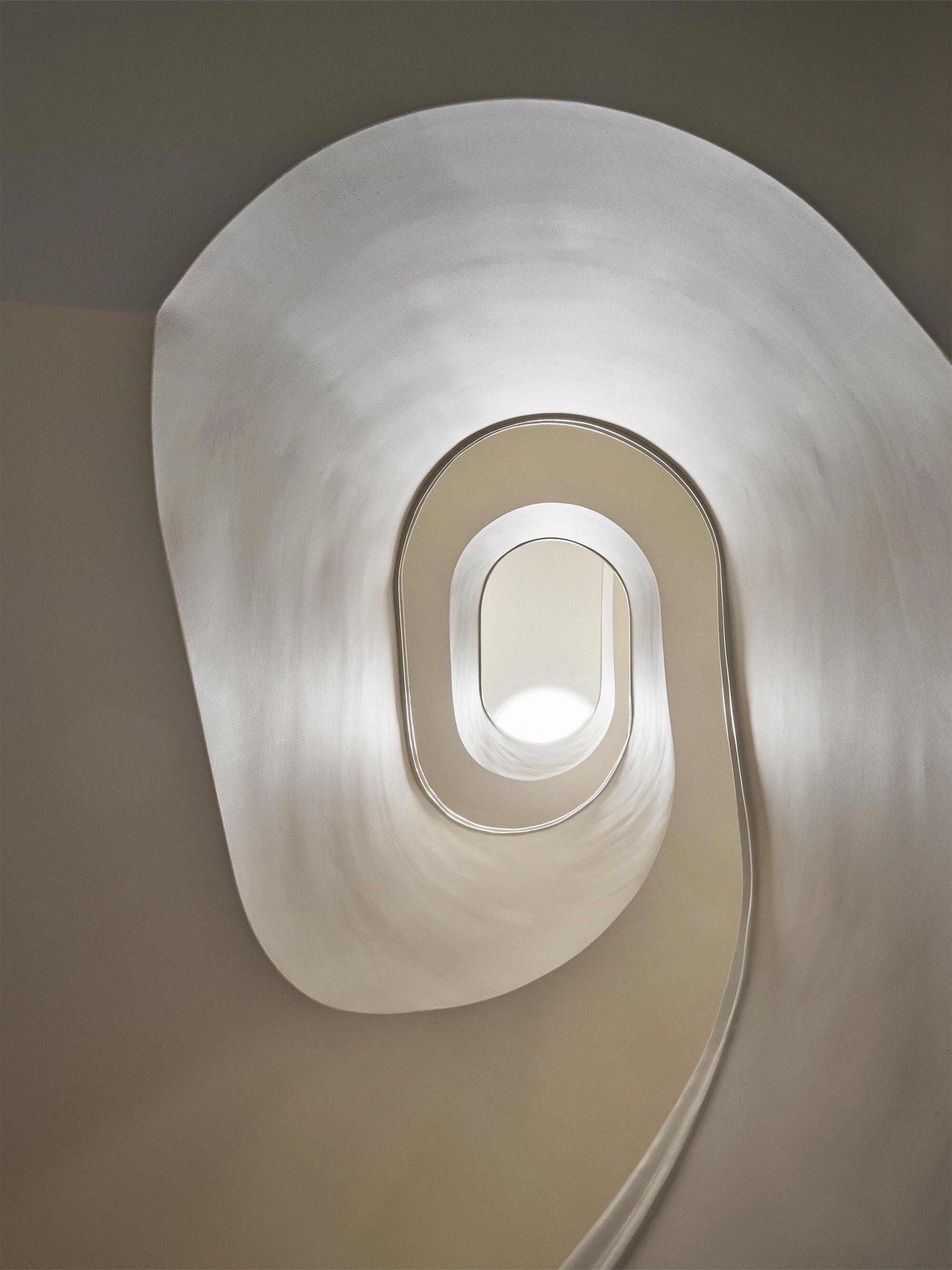 Looking up through an oval-shaped spiral stairwell with smooth plaster walls in natural light