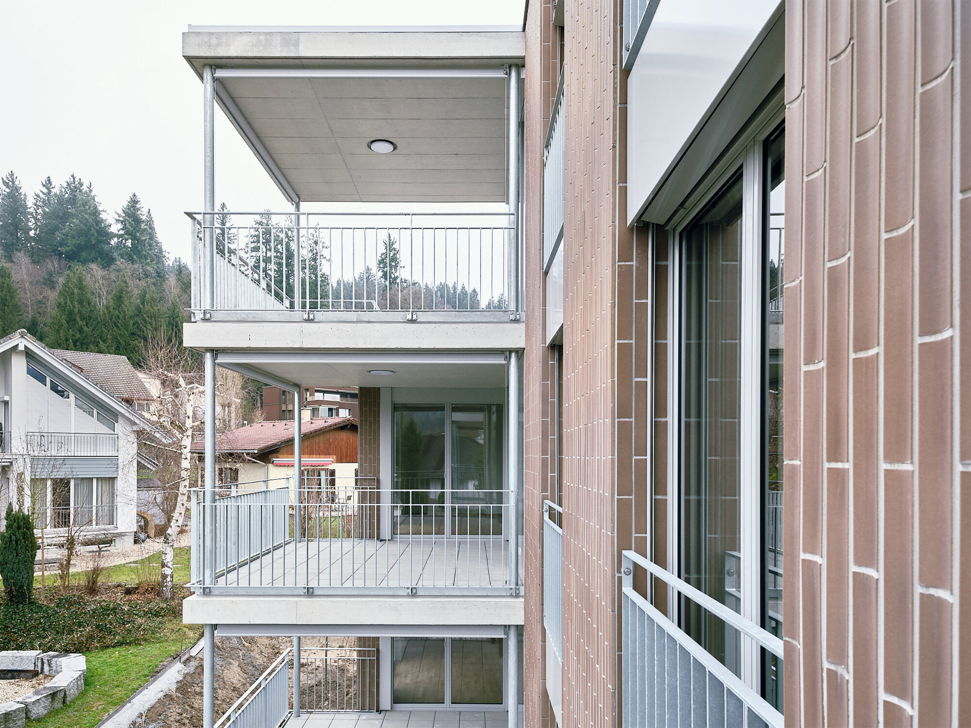 Side view of the recessed balconies with white railings overlooking neighboring houses and trees