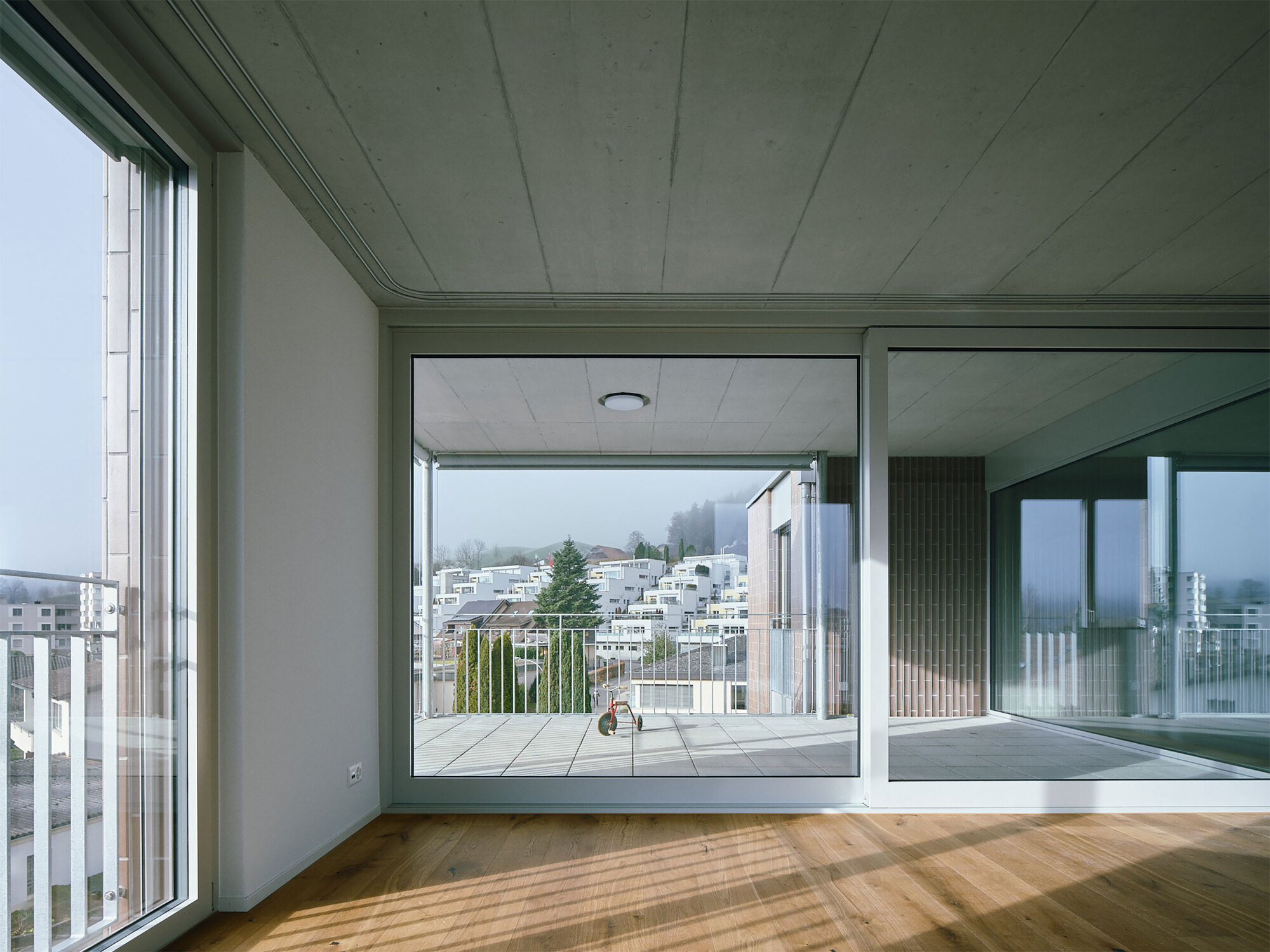 Living room with floor-to-ceiling glazing framing a tiled balcony and distant hills in mist