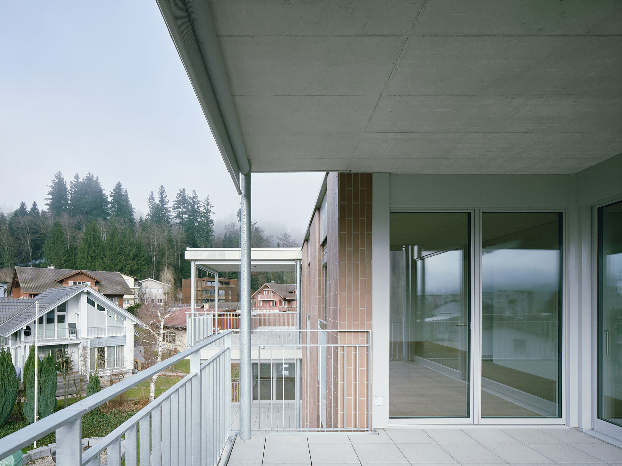 Recessed balcony with concrete soffit and timber cladding column facing a forested hillside