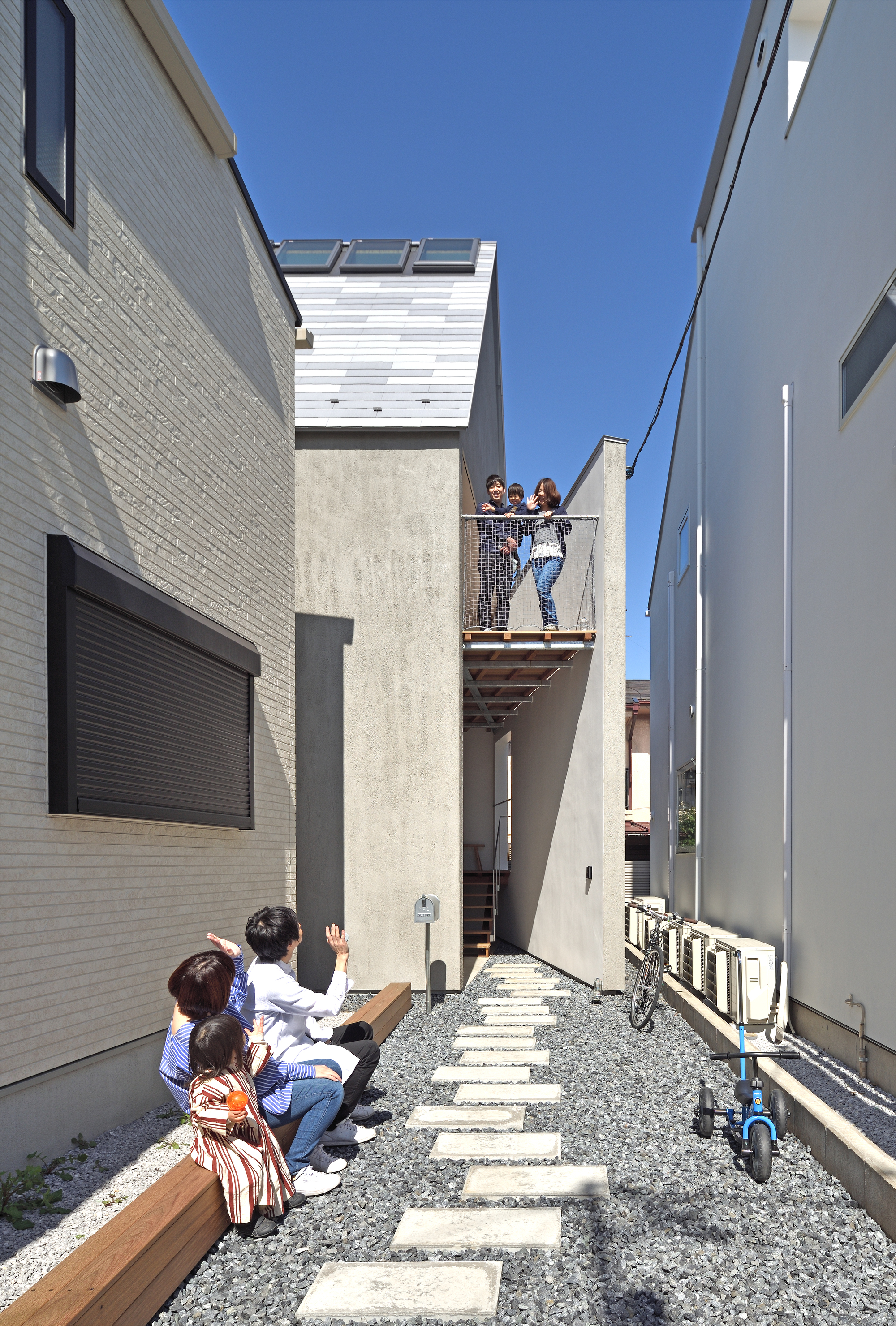 Narrow side courtyard with stepping stone path where residents gather below a cantilevered balcony