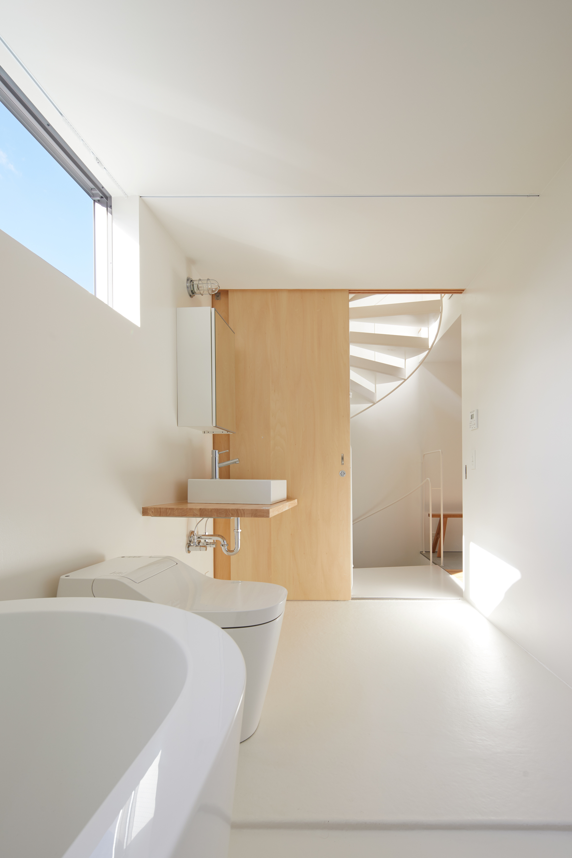 Bathroom with timber partition and floating sink looking toward the spiral staircase beyond