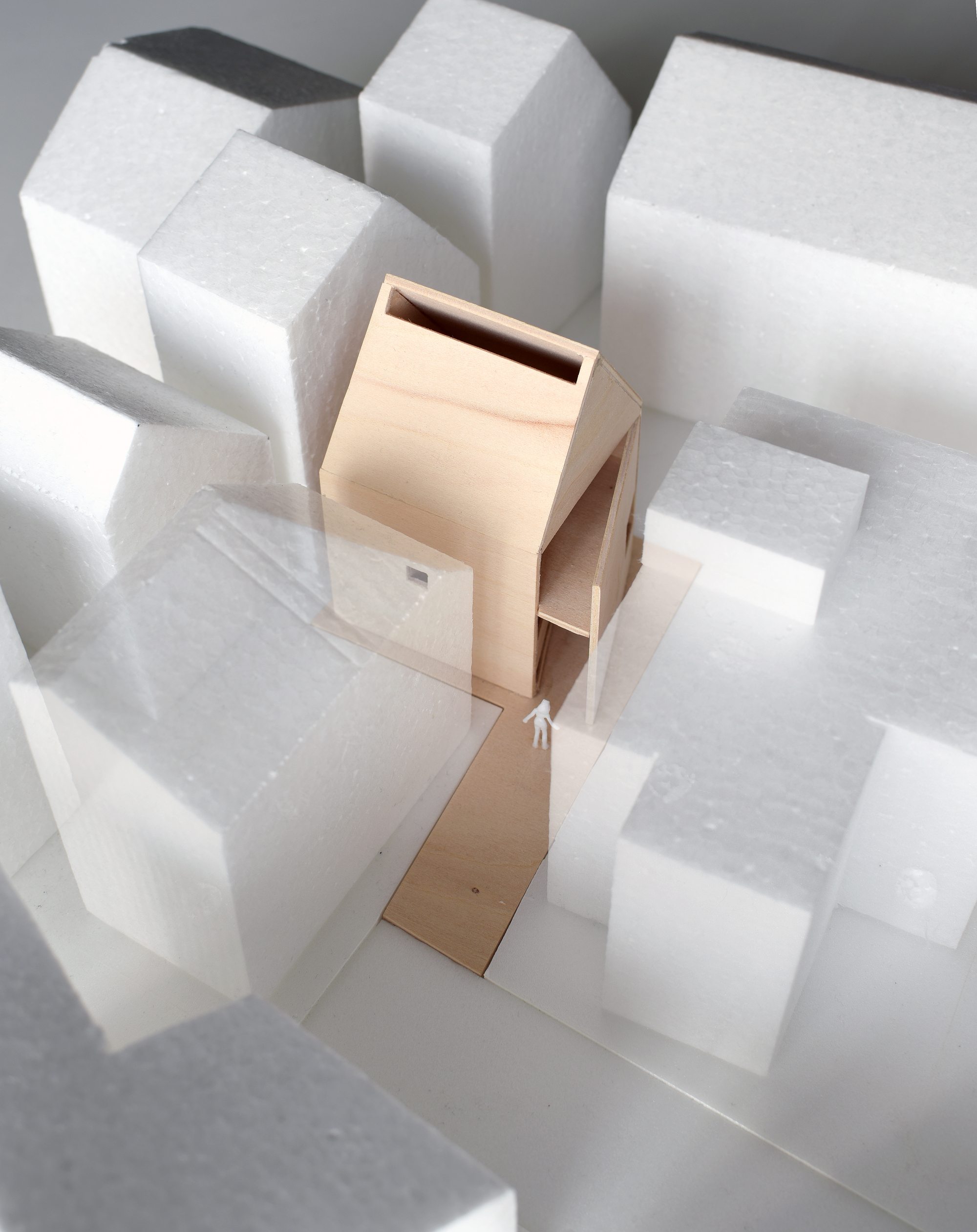 Physical model of a slender timber house form surrounded by white foam block massing