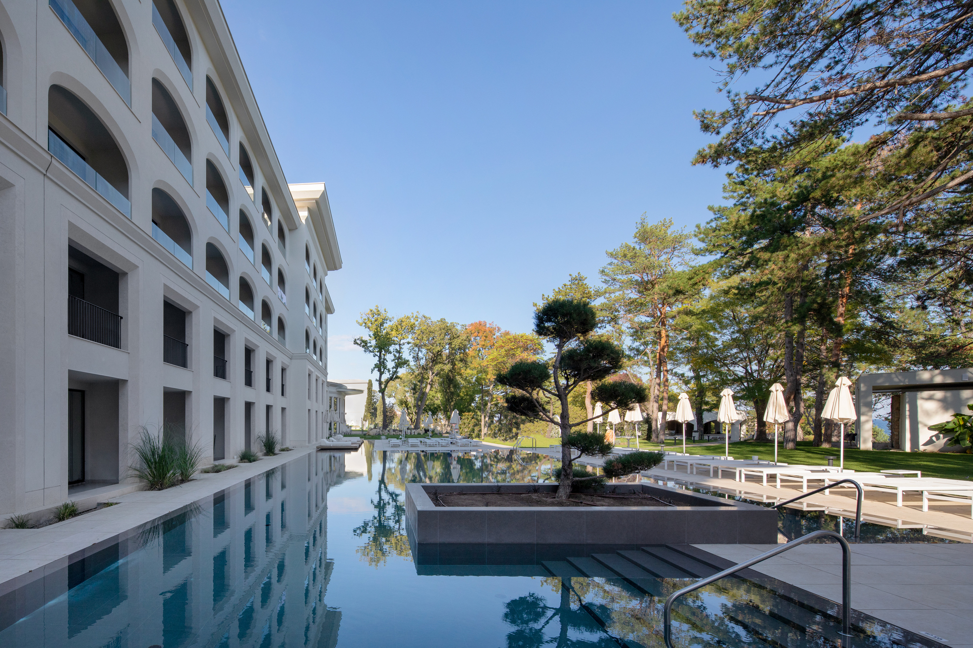 Reflecting pool running alongside the white facade with arched openings and planted courtyard
