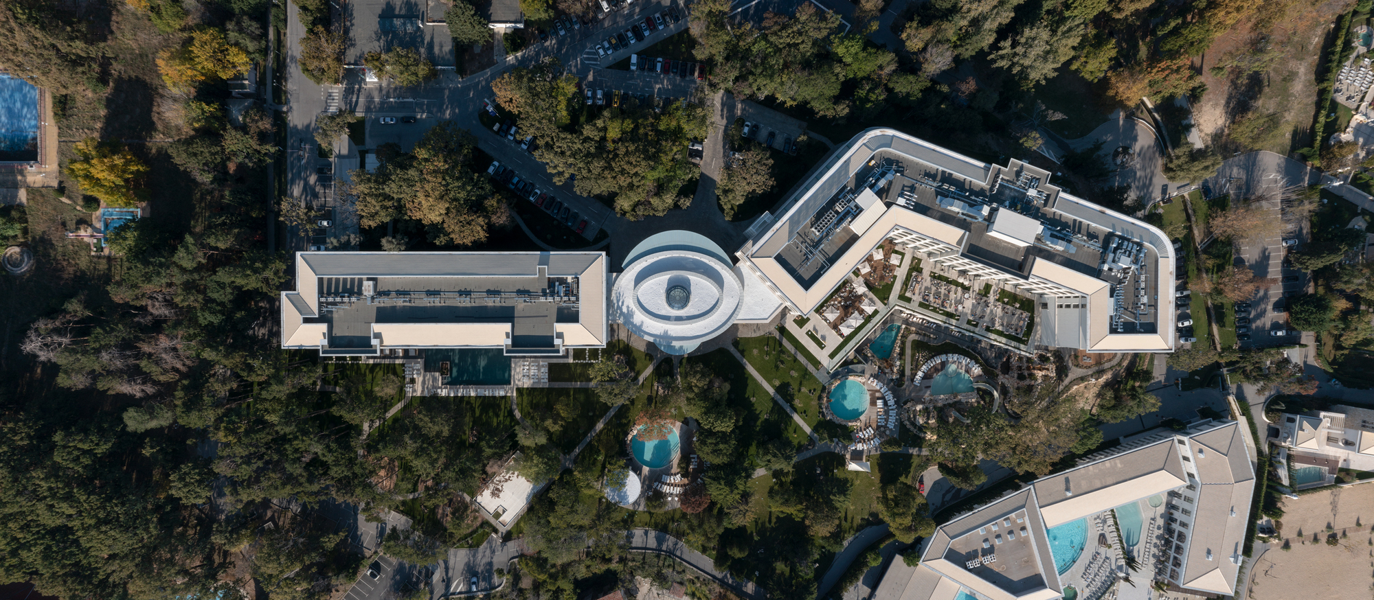 Drone view of the complex showing curved rooftops, circular courtyard and surrounding forest