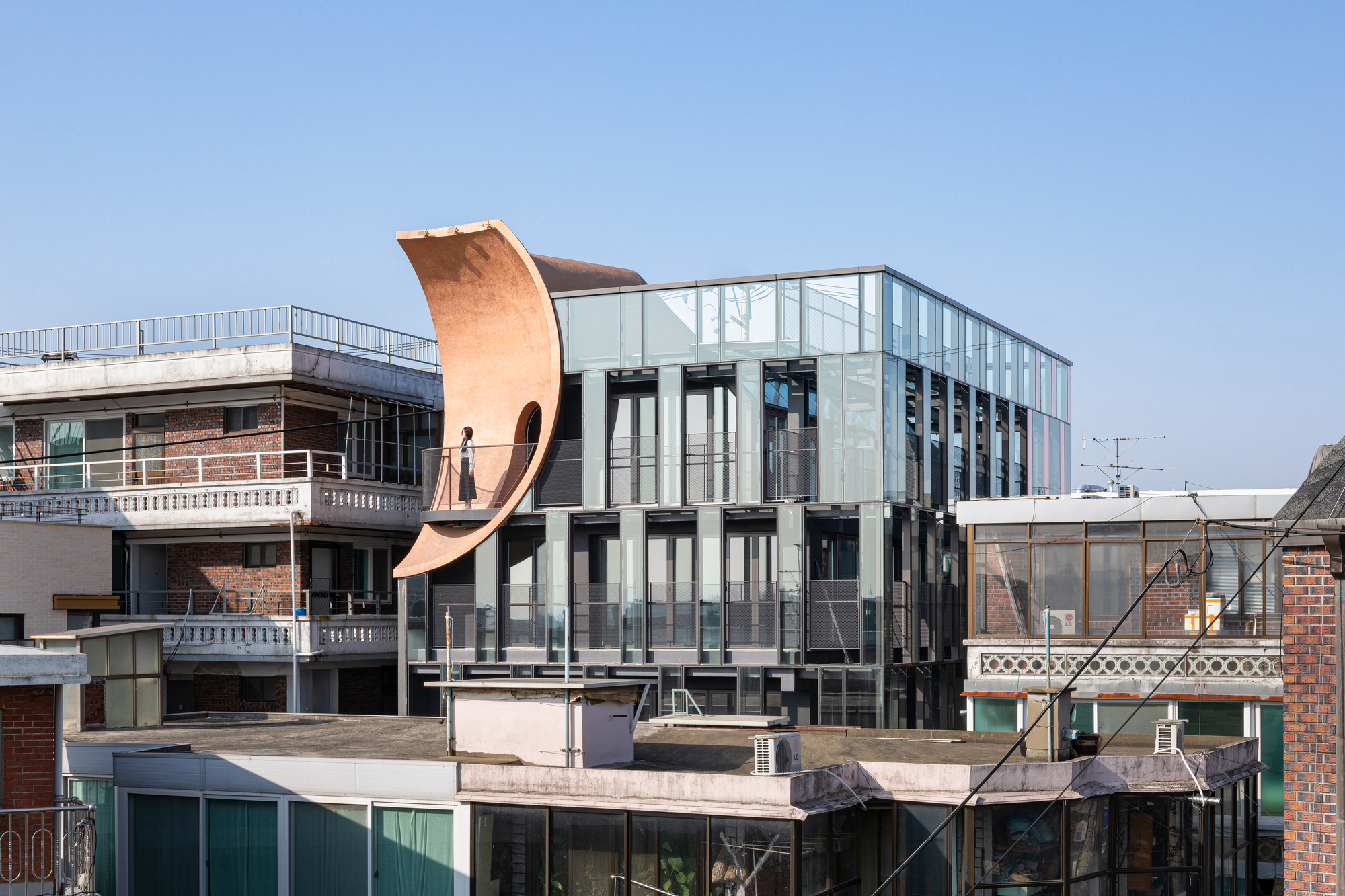 Rooftop view showing the curving copper-toned element rising above the glazed rear elevation