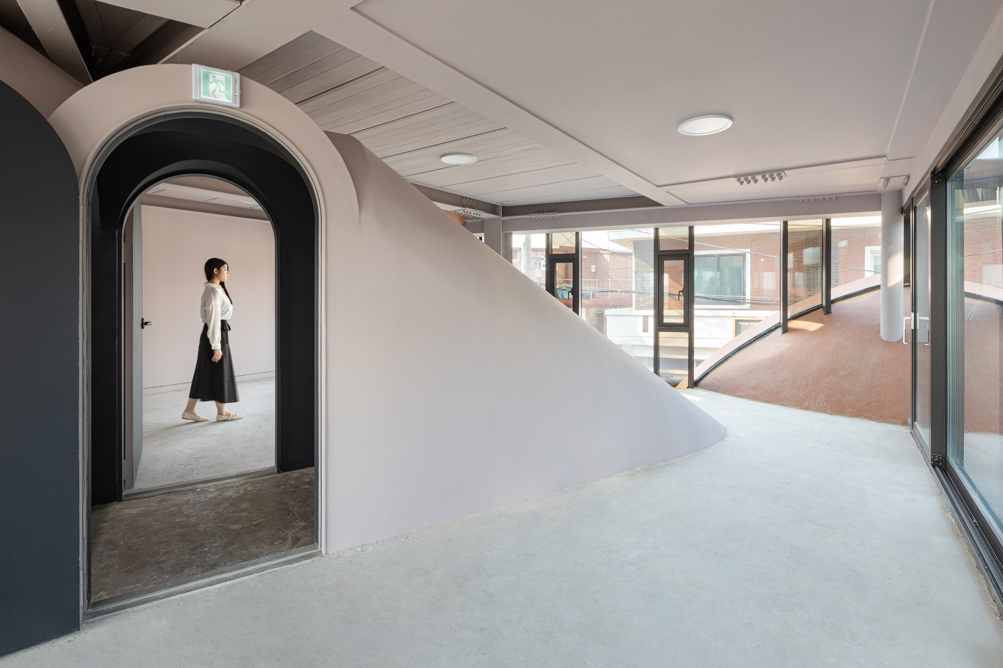 Interior with arched doorway framing a figure and glazed corridor beyond