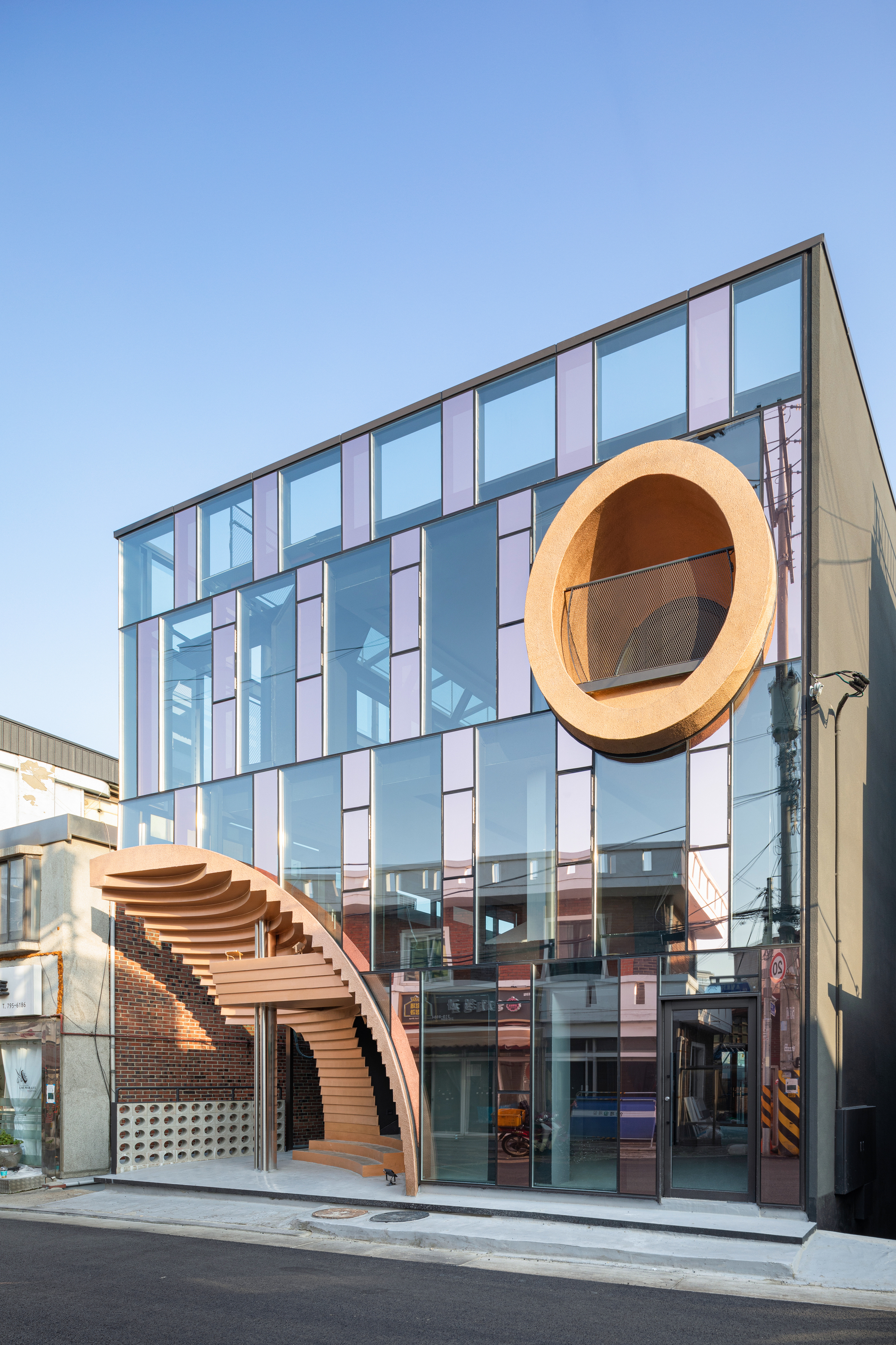 Corner elevation showing the circular timber volume and stepped canopy against a clear sky