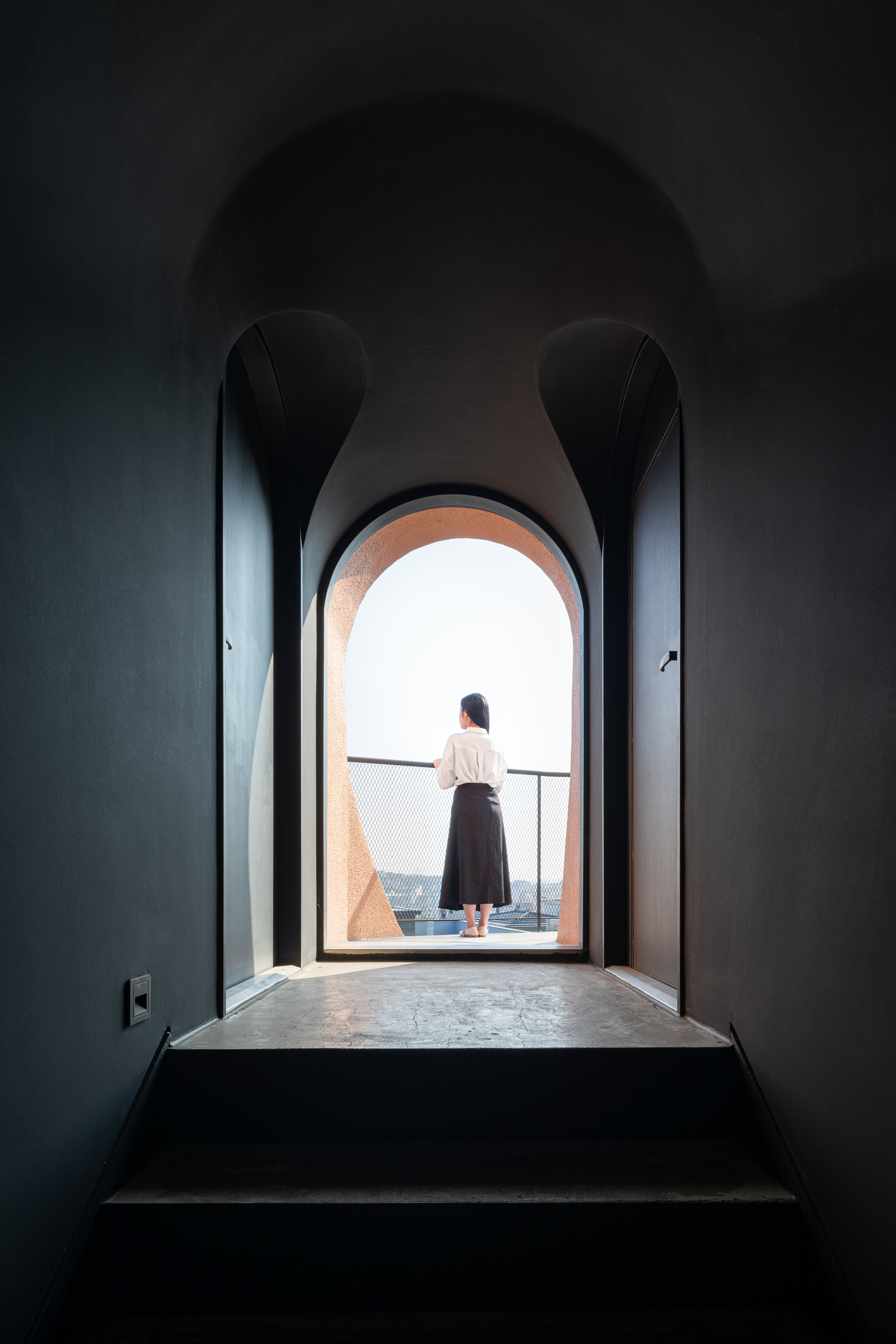 Dark arched corridor with a person standing at the illuminated opening overlooking the cityscape