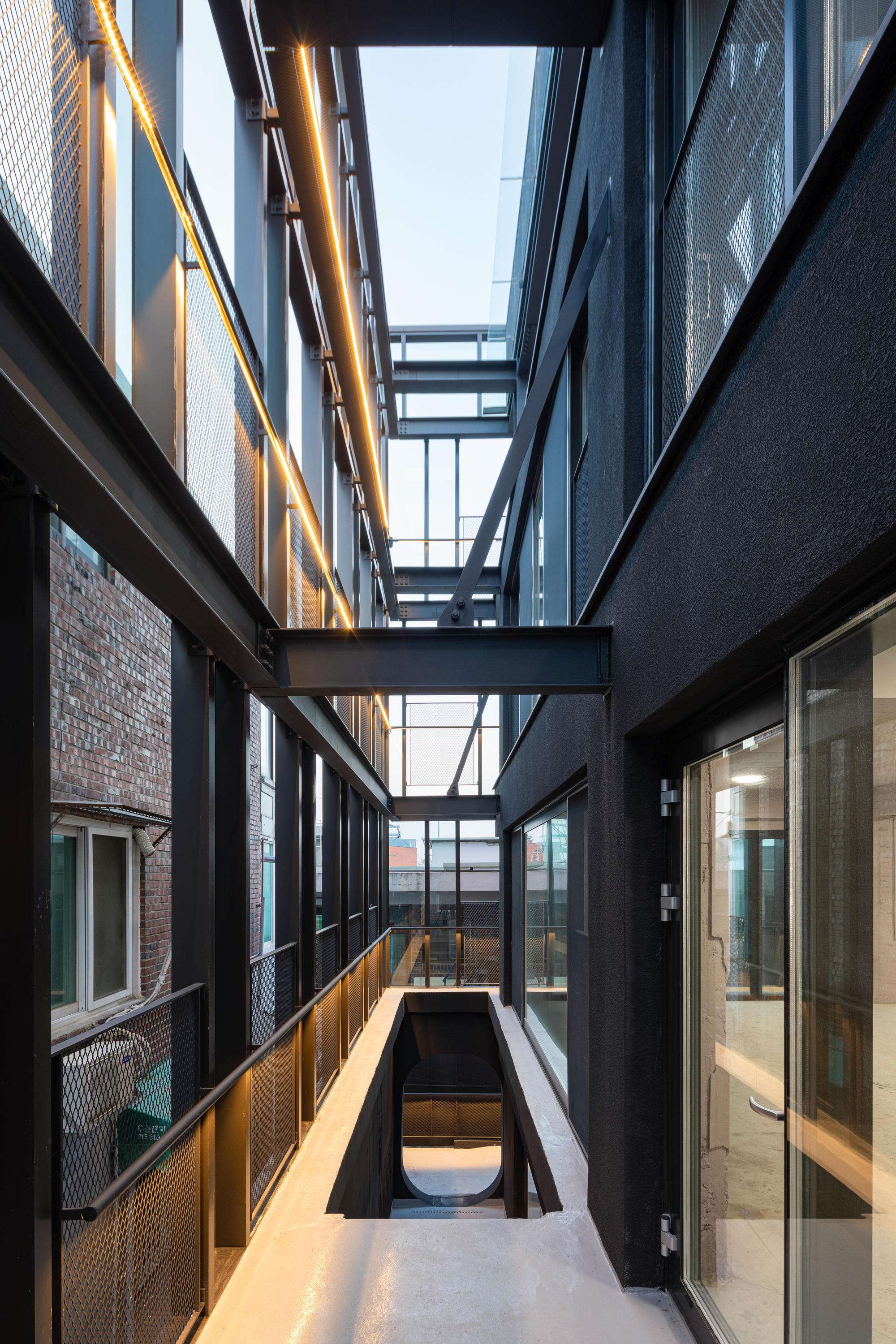 Narrow courtyard between black facades with overhead bridges and a glazed skylight above