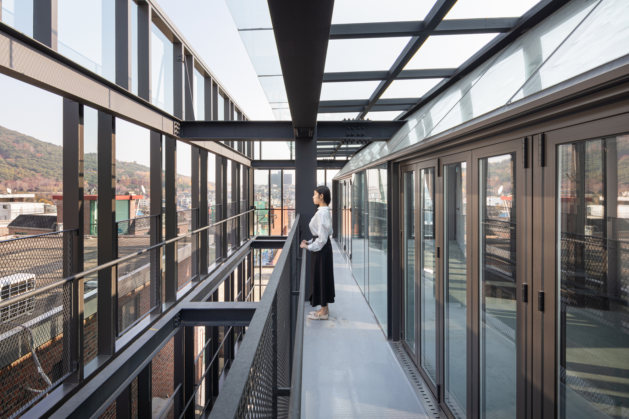 Exterior walkway with perforated metal balustrade and black steel overhead beams at dusk