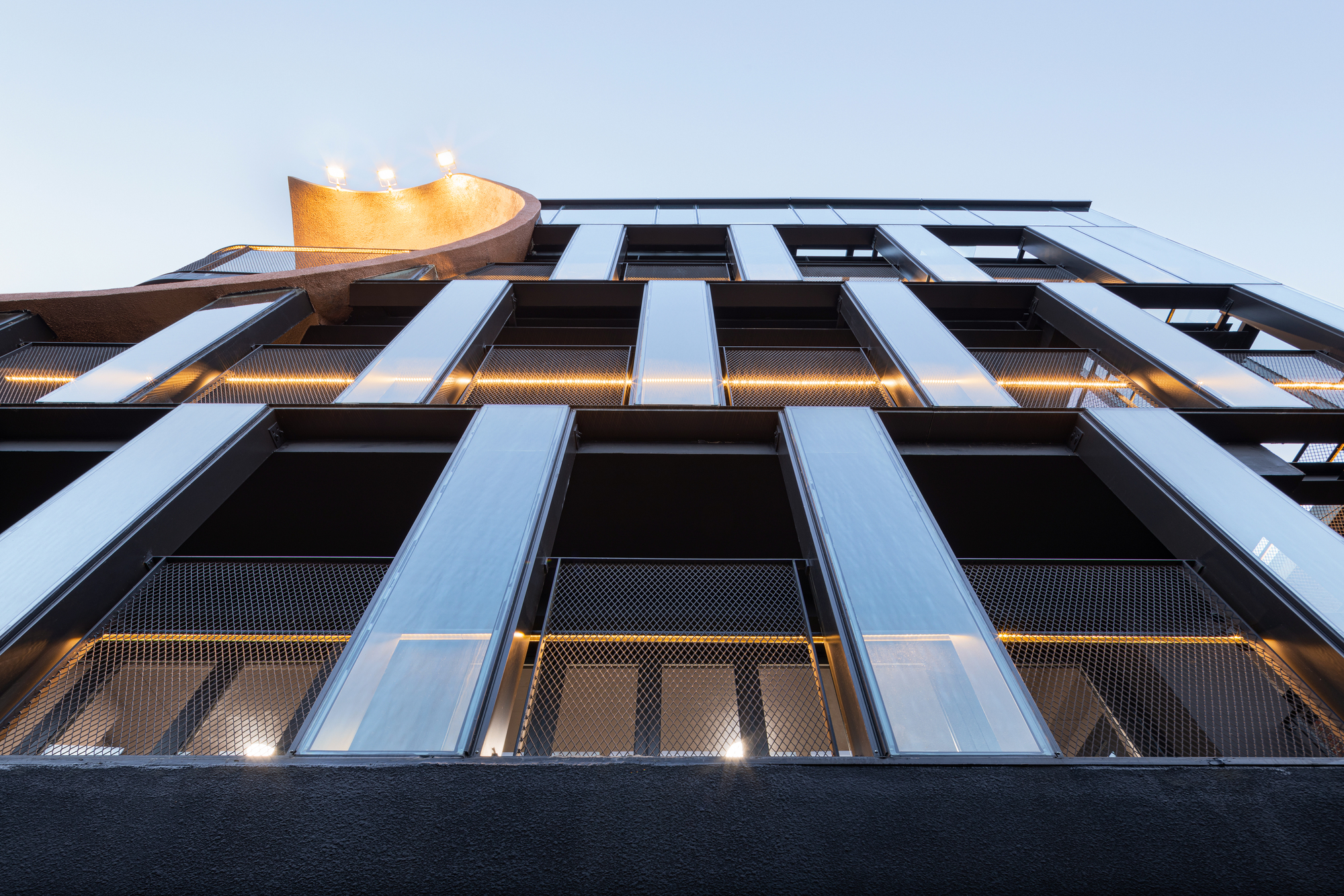 Upward view of the black metal and perforated mesh facade at twilight
