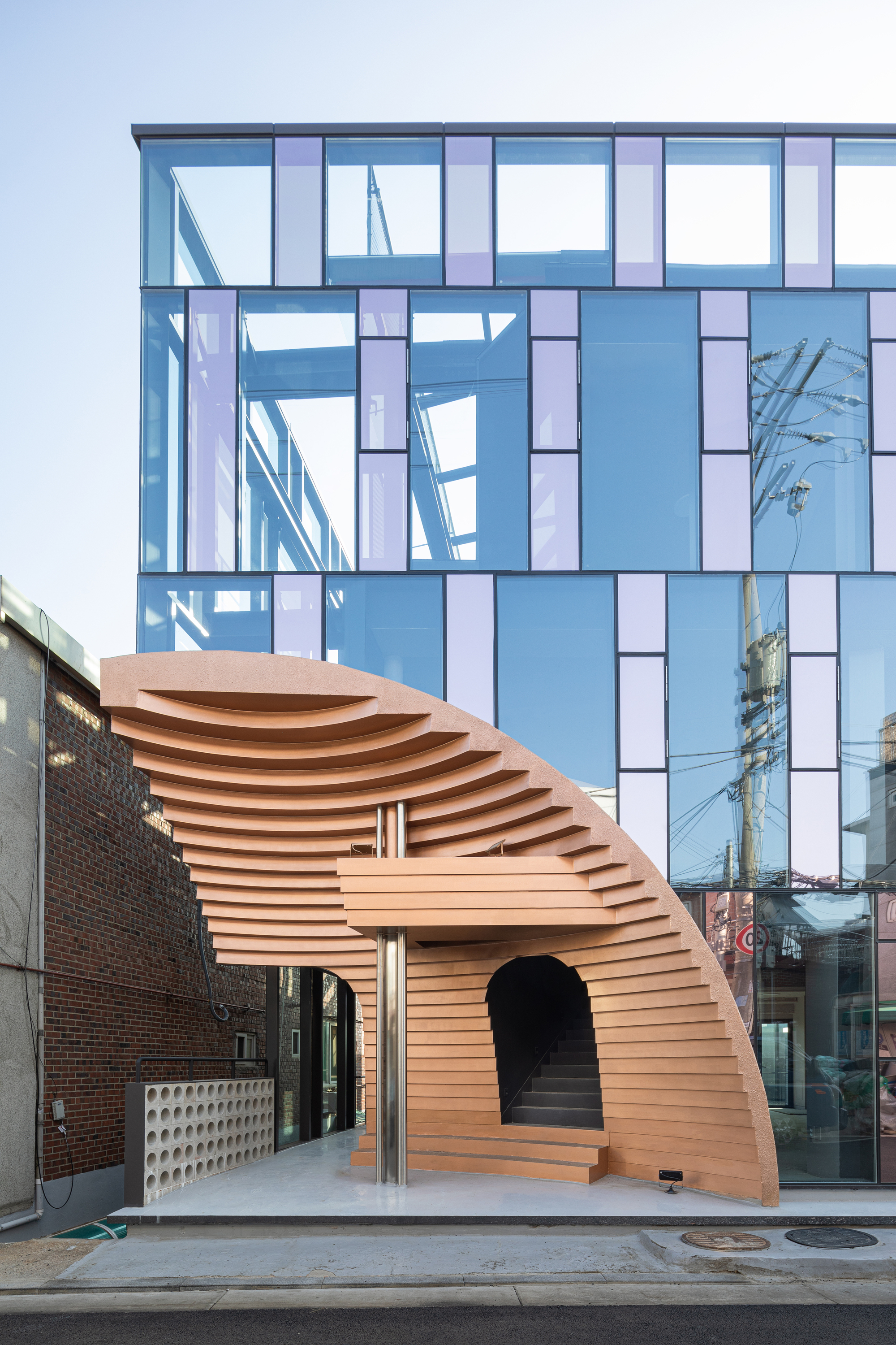 Curved timber entry pavilion with horizontal slats beneath a glazed curtain wall